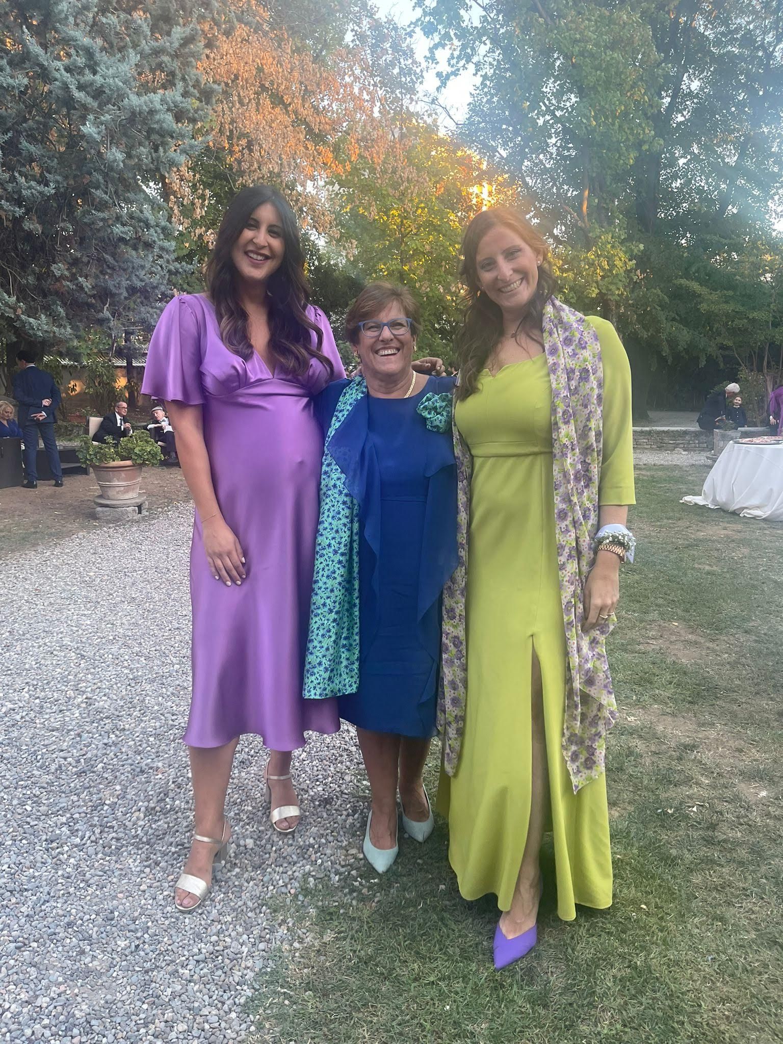 Tre donne in abito elegante posano insieme per una foto.