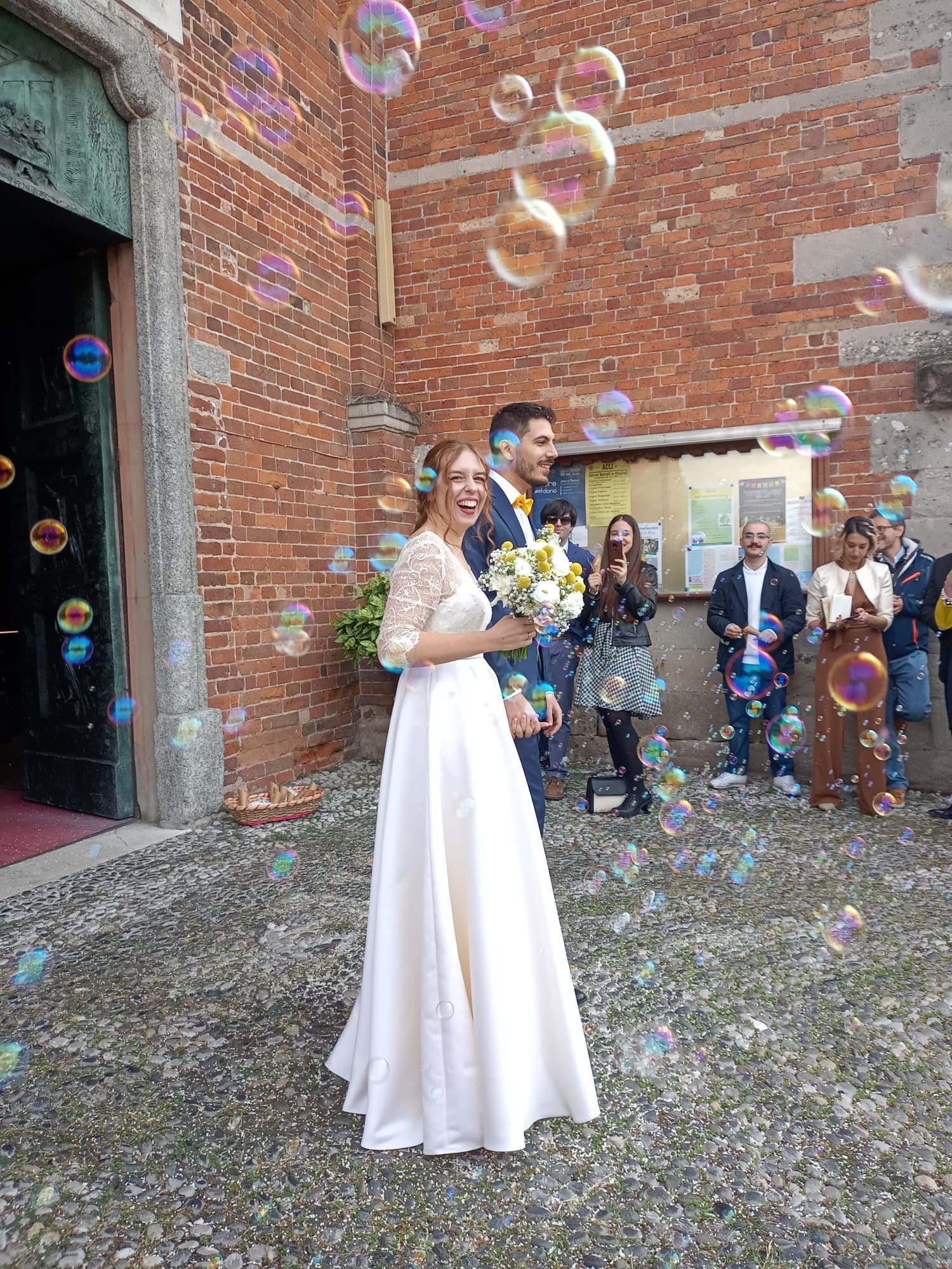 Una coppia di sposi è in piedi davanti a una chiesa, circondati da bolle di sapone.