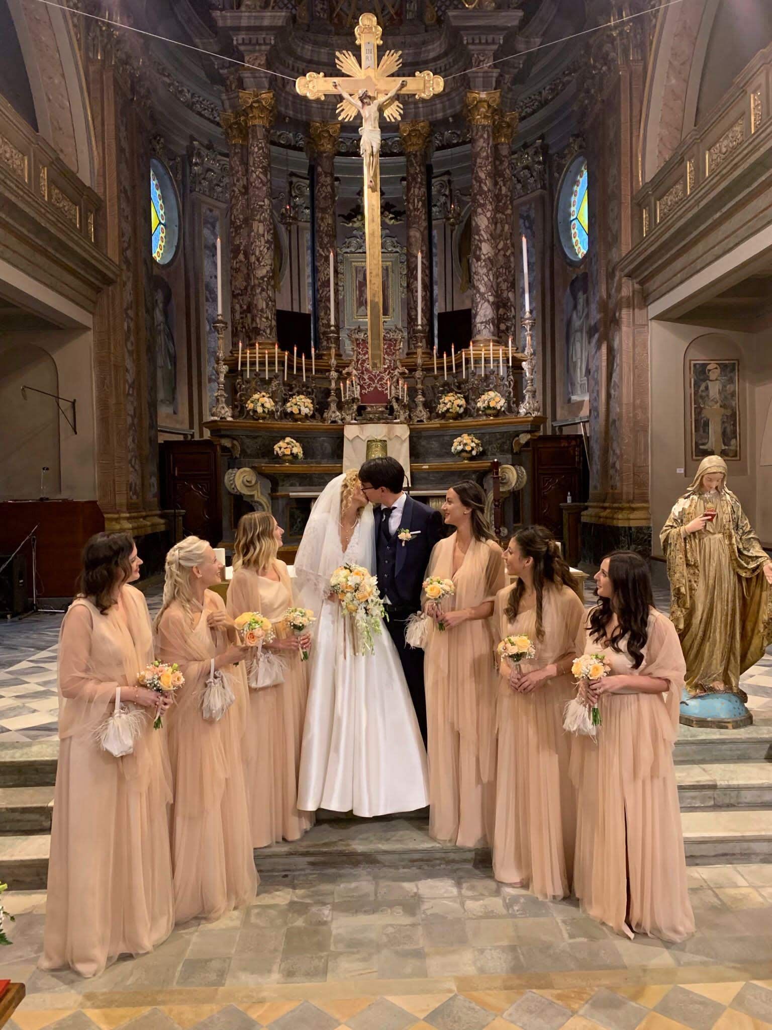 Una sposa e uno sposo si baciano davanti alle loro damigelle in una chiesa.