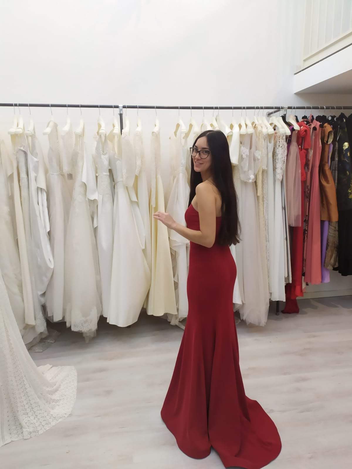 Una donna con un vestito rosso è in piedi davanti a uno scaffale di vestiti bianchi.