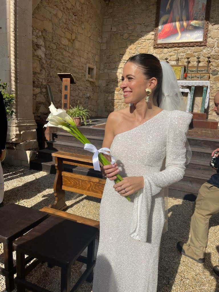Una sposa in abito bianco tiene in mano un mazzo di fiori davanti a una chiesa.