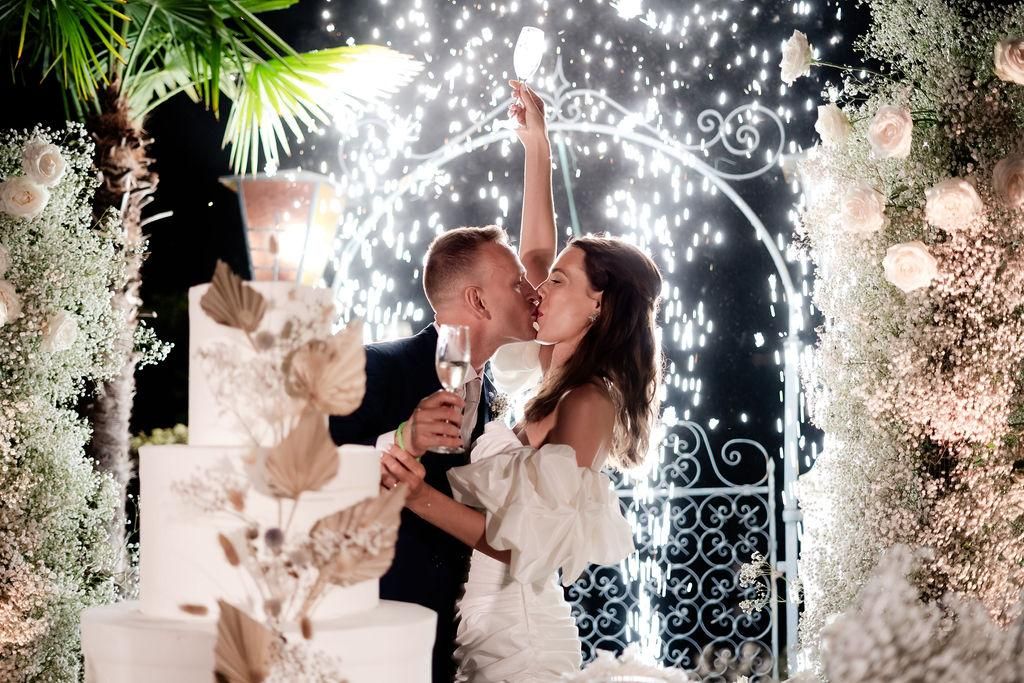 Una sposa e uno sposo si baciano davanti a una torta nuziale.