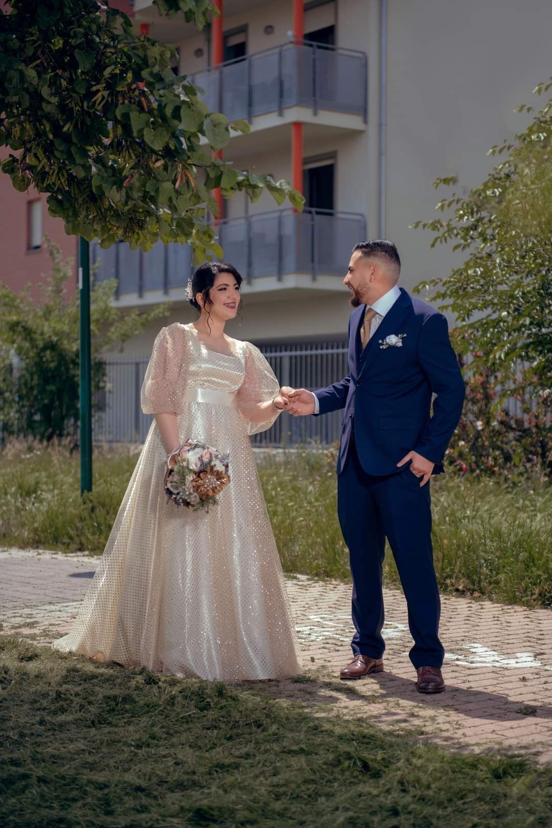 Una sposa e uno sposo sono in piedi uno accanto all'altro in un parco e si tengono per mano.