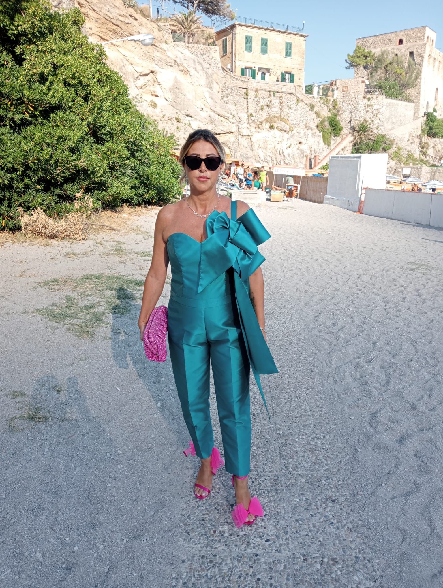 Una donna con un vestito blu e scarpe rosa è in piedi su una strada sterrata.