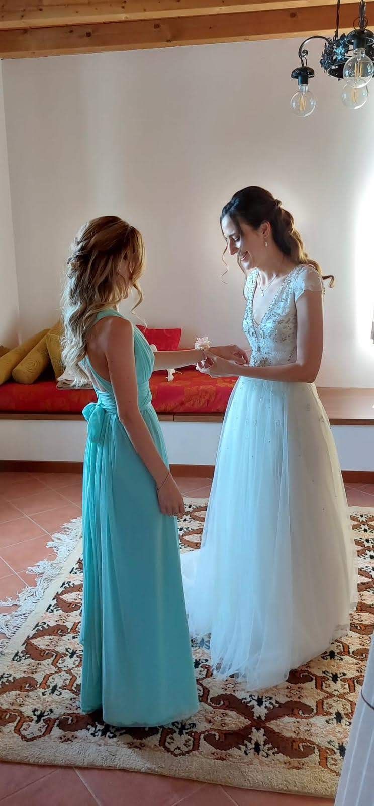 Una sposa e la sua damigella sono in piedi una accanto all'altra in una stanza.