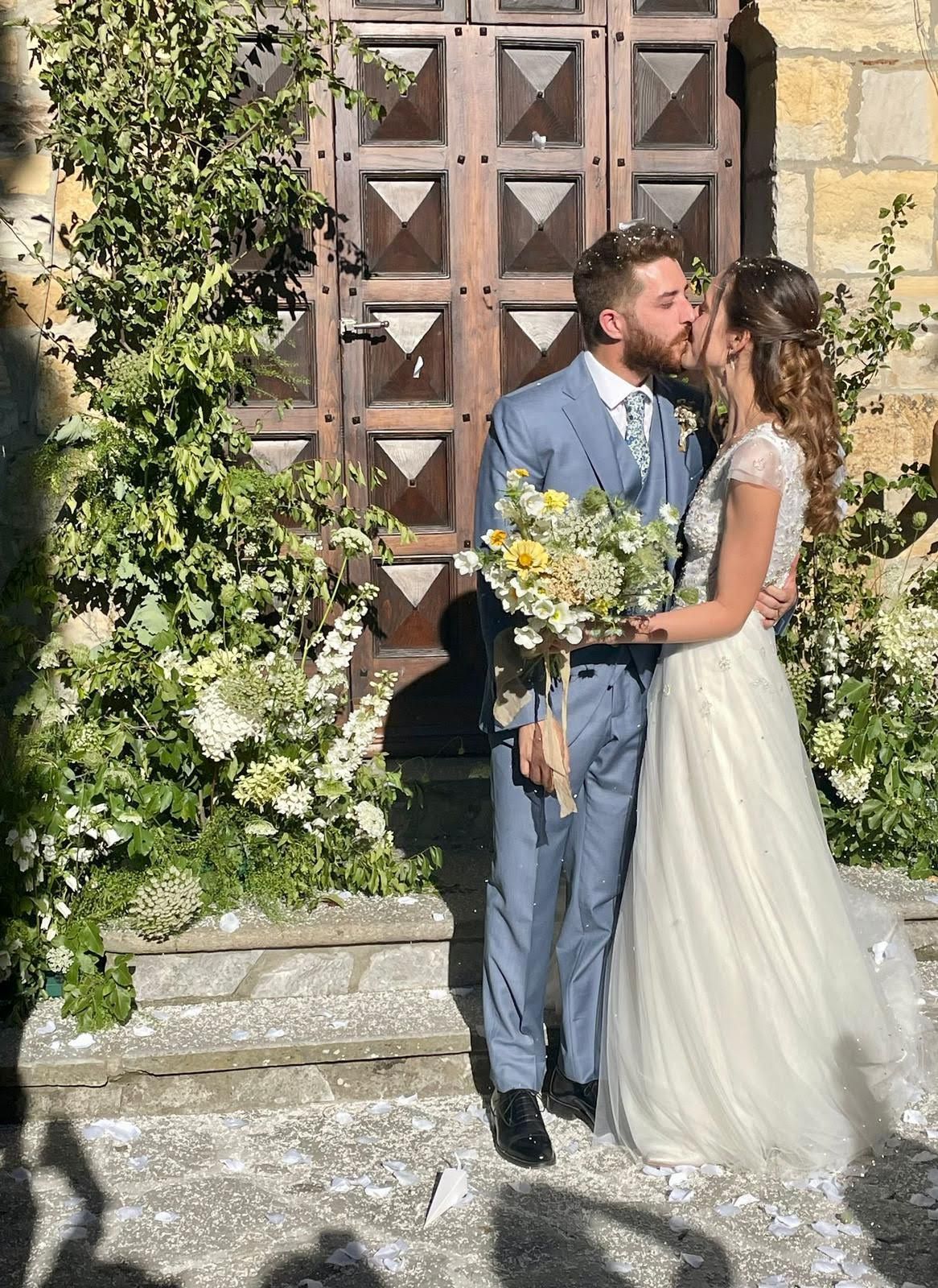 Una sposa e uno sposo si baciano davanti a una porta di legno.