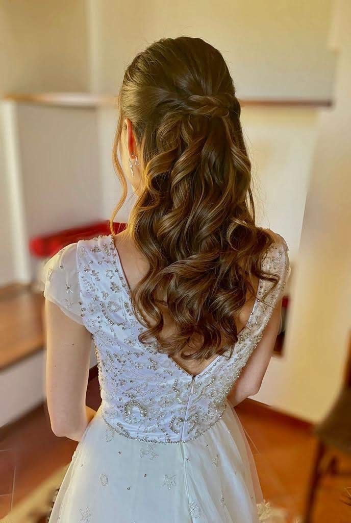 La schiena di una donna in abito da sposa con i capelli raccolti in una coda di cavallo mezza su e mezza giù.