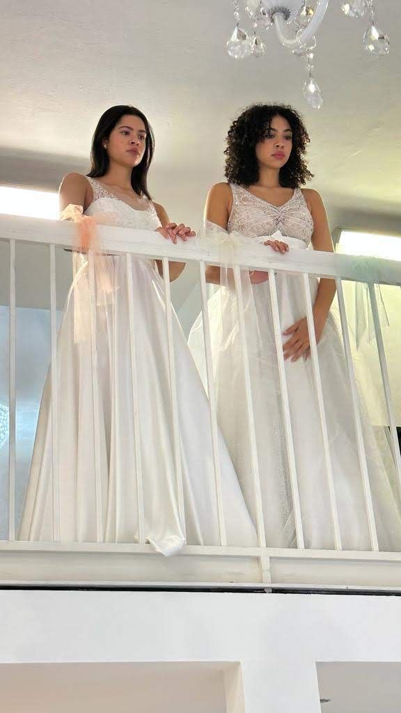 Due donne in abiti bianchi sono in piedi una accanto all'altra su un balcone.