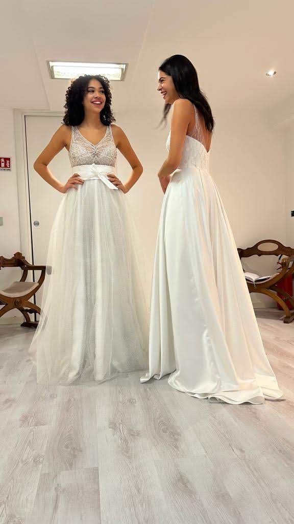 Due donne in abito da sposa sono in piedi una accanto all'altra in una stanza.