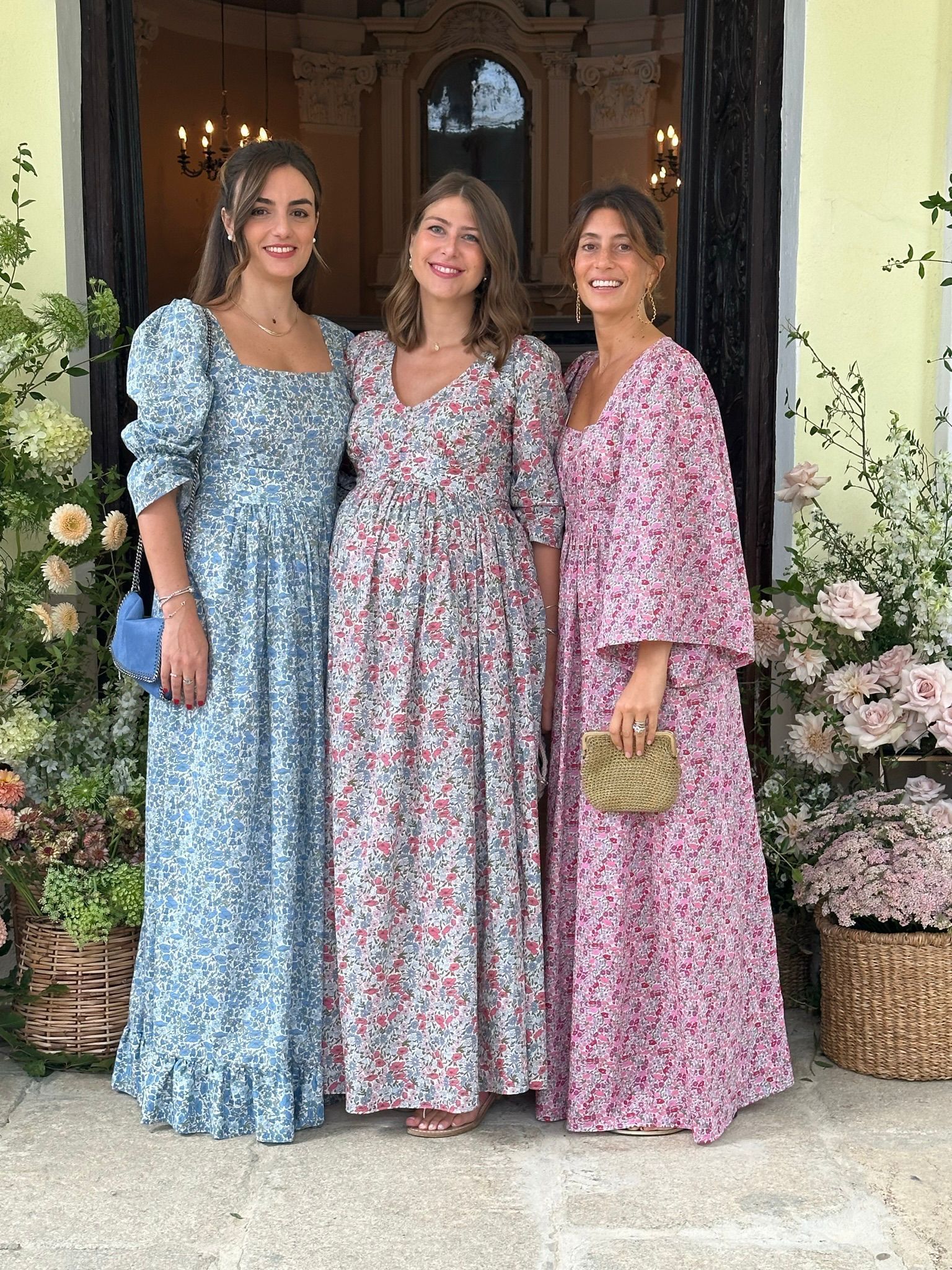 Tre donne in abiti lunghi sono in piedi una accanto all'altra davanti a una porta.