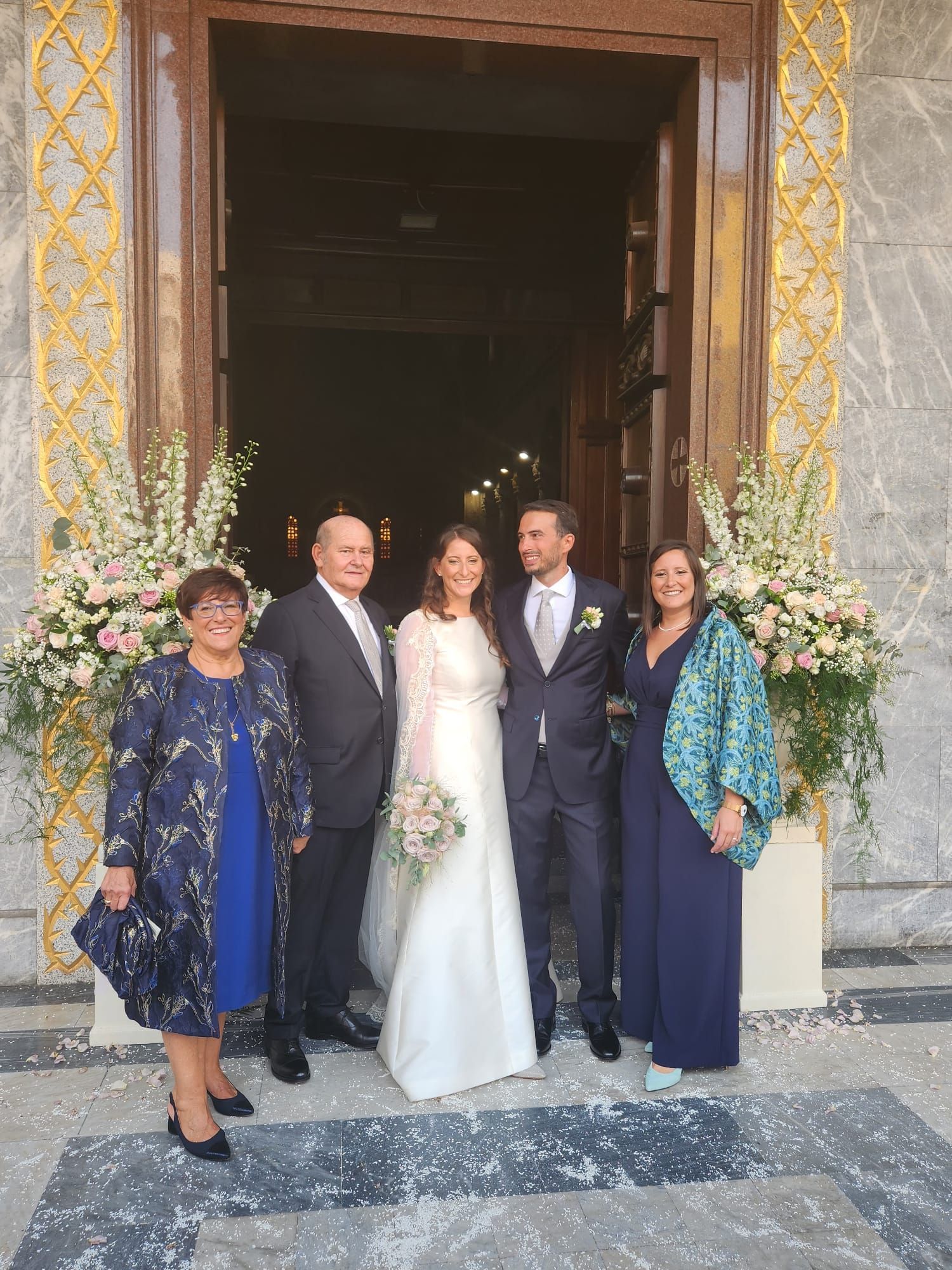 Una coppia di sposi posa per una foto con la propria famiglia fuori da una chiesa.