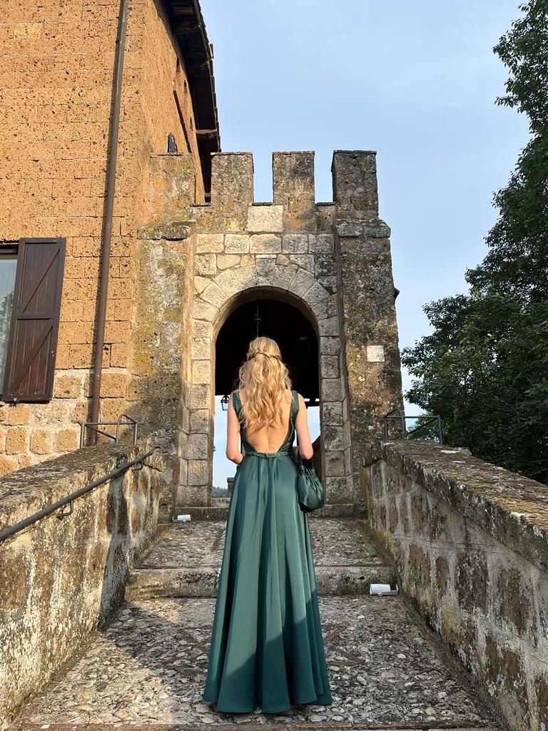 Una donna con un vestito verde è in piedi davanti a un edificio in pietra.