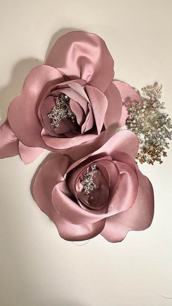 Due rose rosa con strass sono su una superficie bianca.