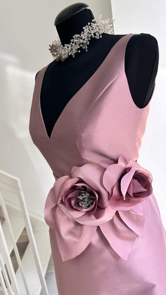 Un vestito rosa con un fiore in vita è su un manichino.