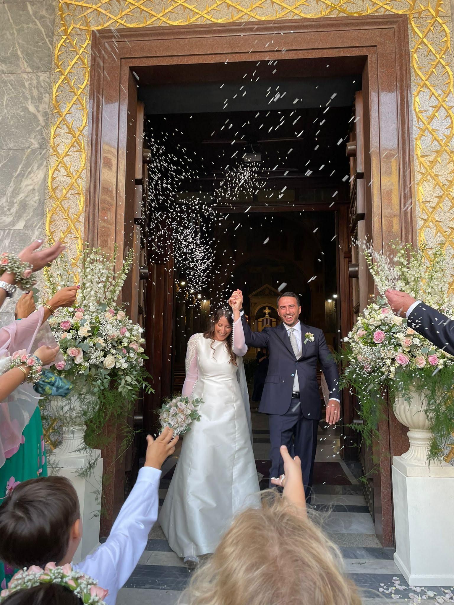 Una coppia di sposi esce da una chiesa circondata da persone che lanciano coriandoli.