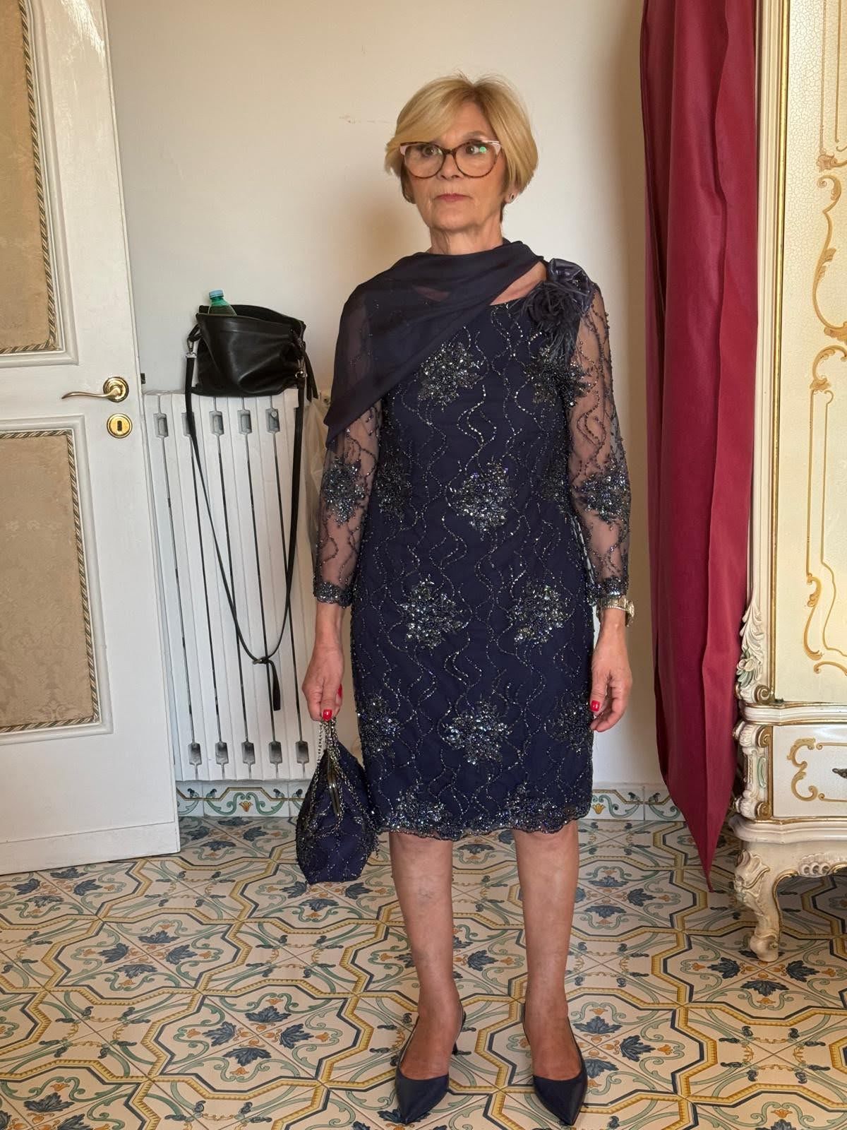 Una donna con un vestito blu e gli occhiali è in piedi in una stanza.