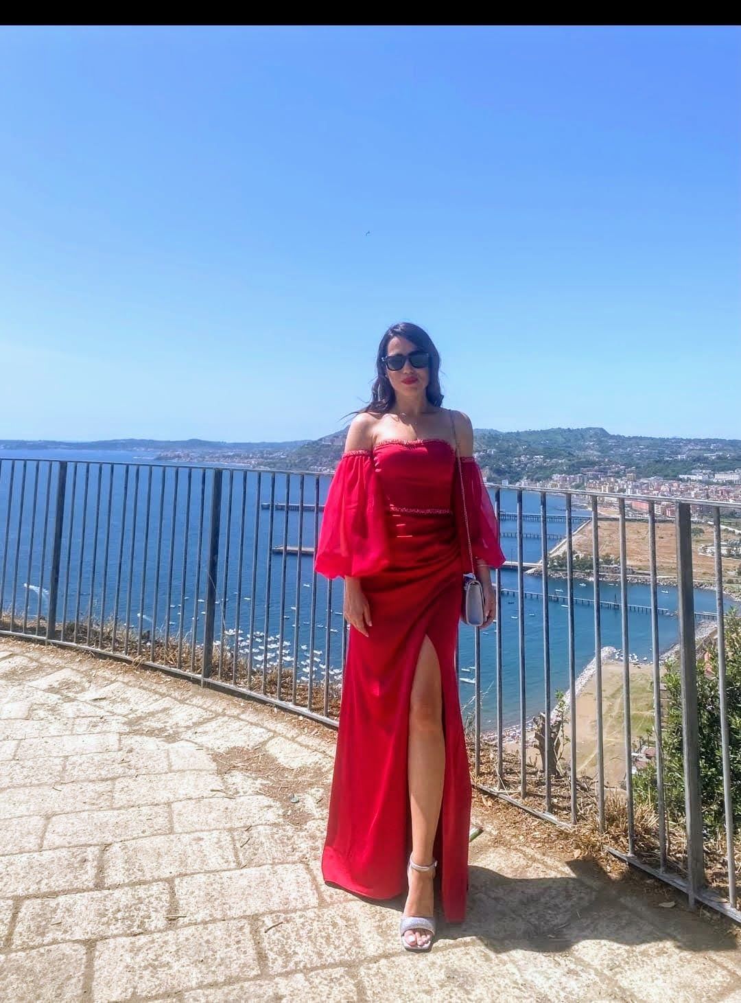 Una donna con un vestito rosso è in piedi davanti a una recinzione che si affaccia sull'oceano.