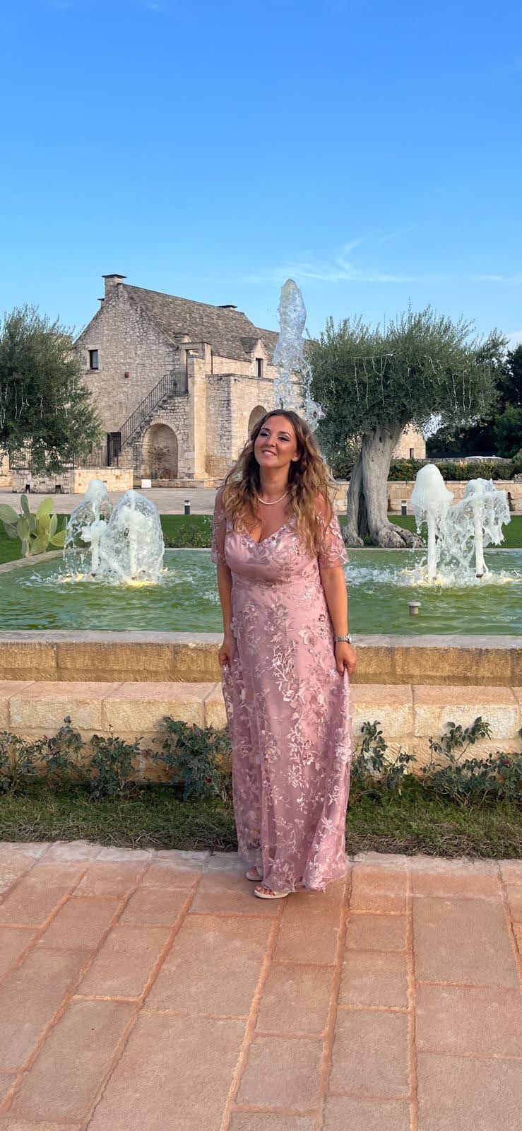 Una donna con un vestito rosa è in piedi davanti a una fontana.