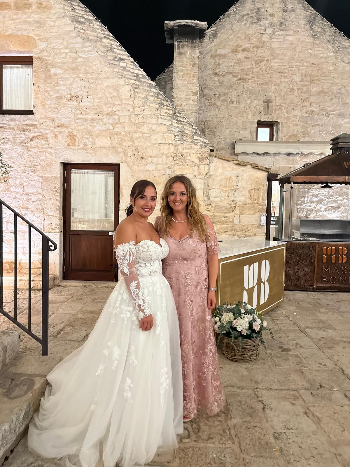 Una sposa e sua madre posano per una foto davanti a un edificio in pietra.