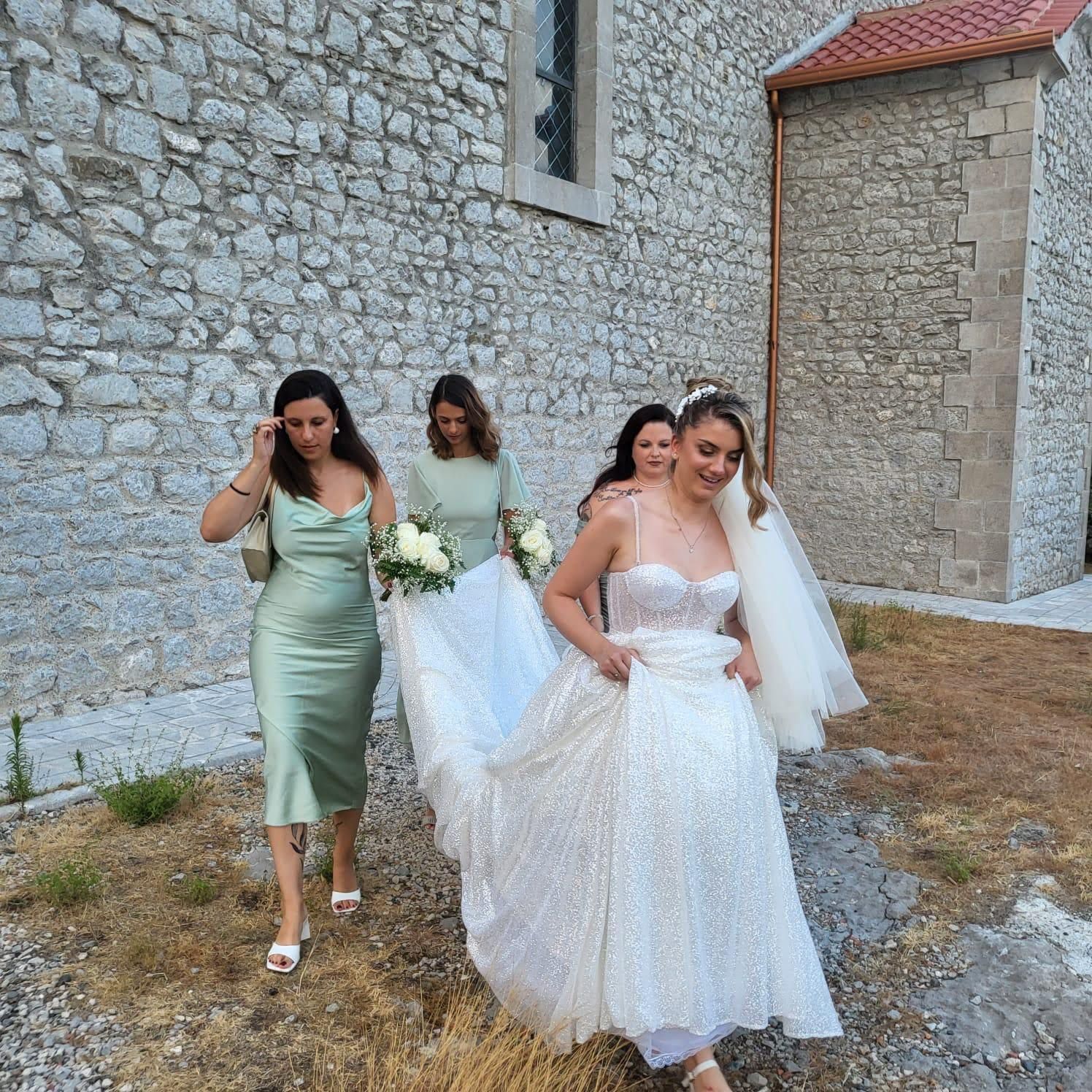Una sposa e le sue damigelle camminano davanti a un edificio in pietra