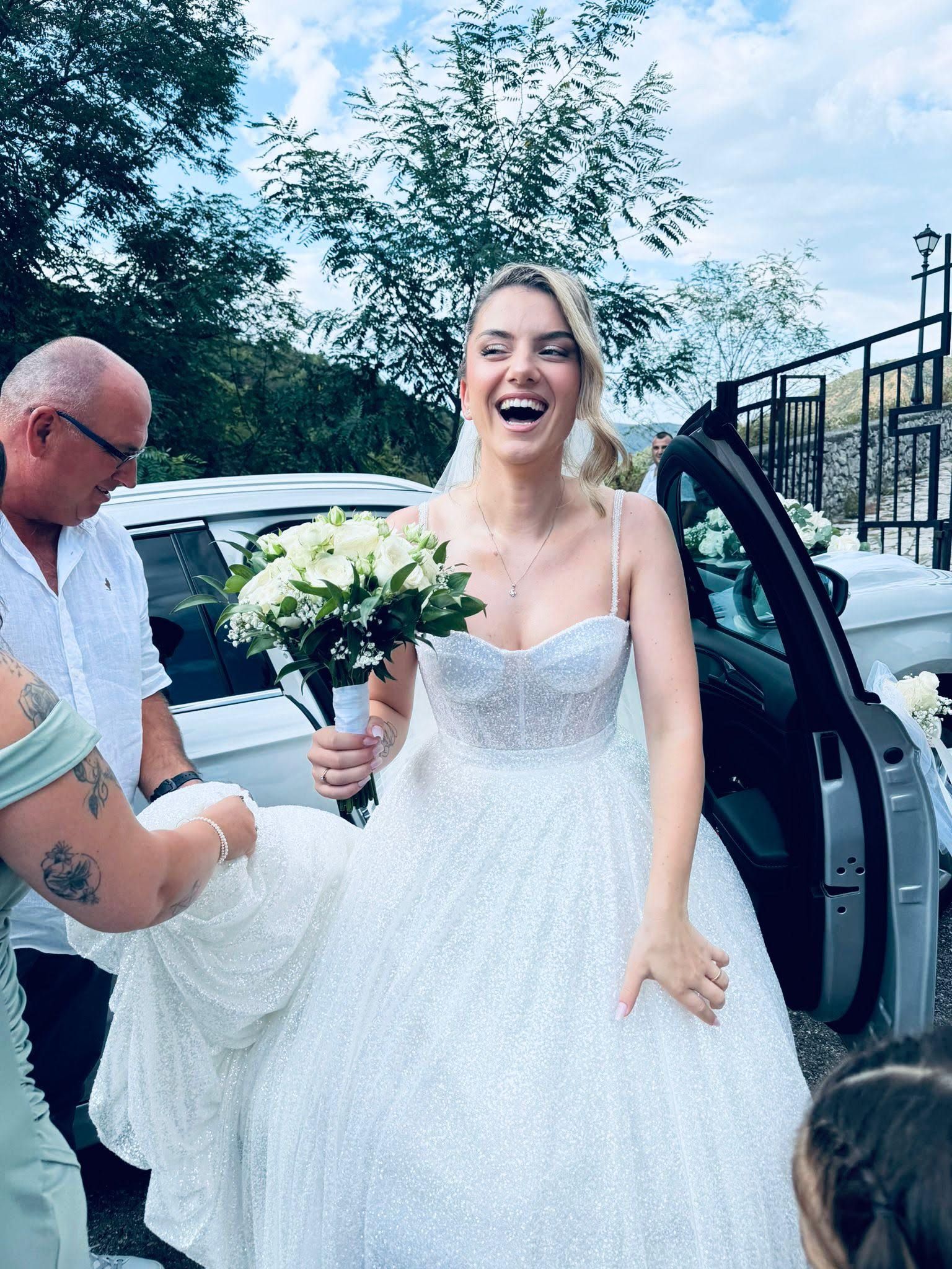 Una sposa in abito da sposa ride mentre scende da un'auto.