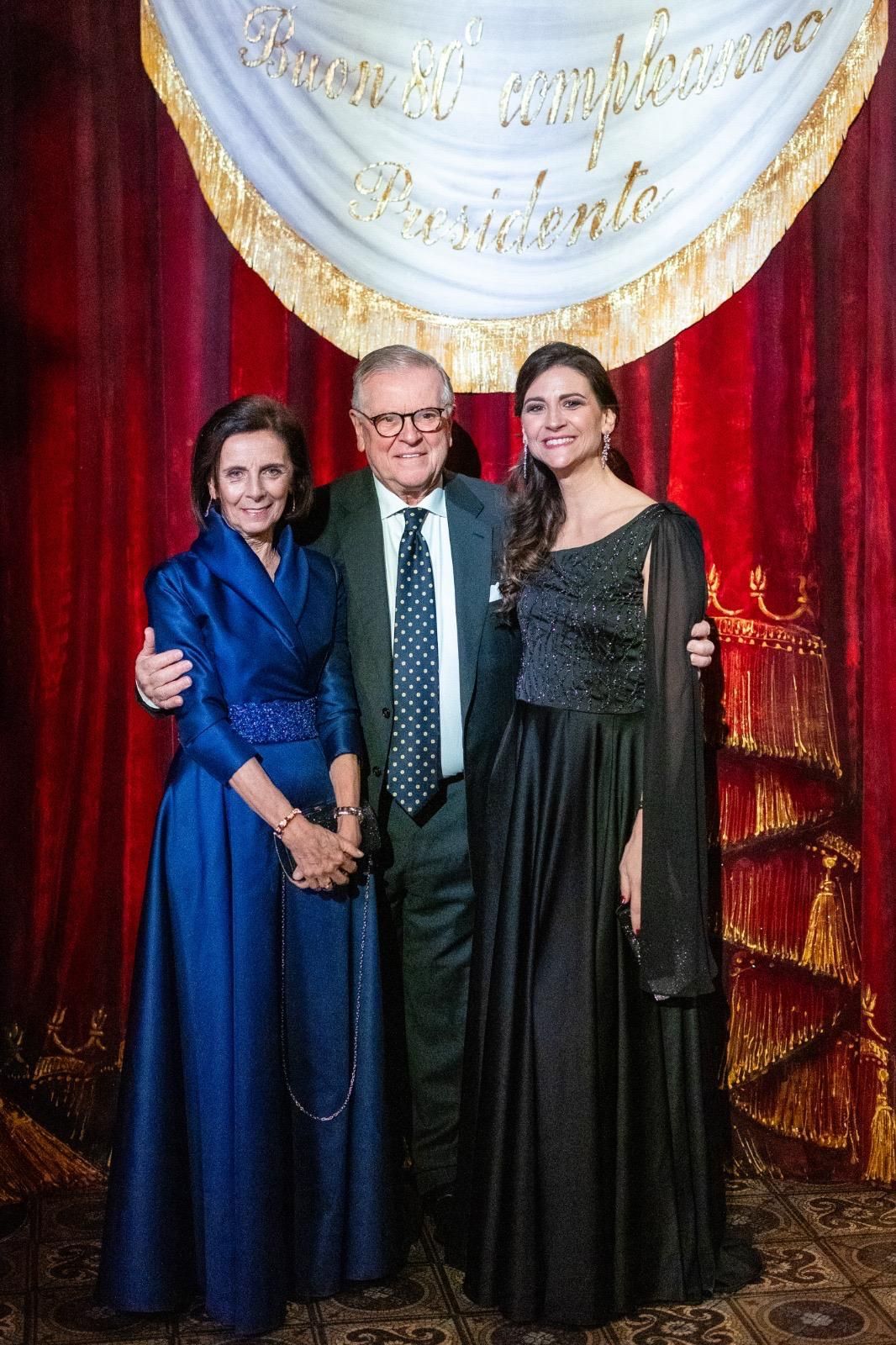 Un uomo e due donne posano per una foto davanti a una tenda rossa.