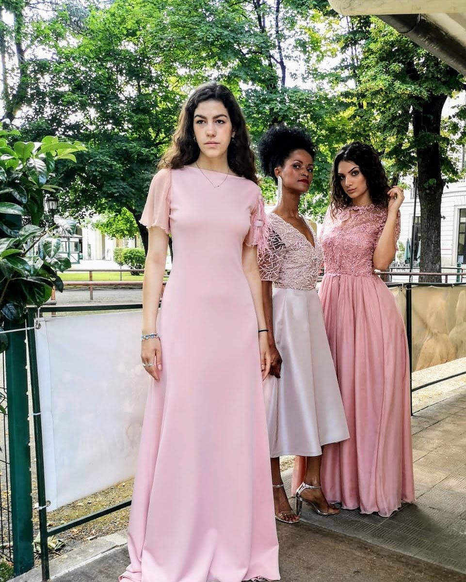 Tre donne in abiti rosa sono in piedi una accanto all'altra su un marciapiede.