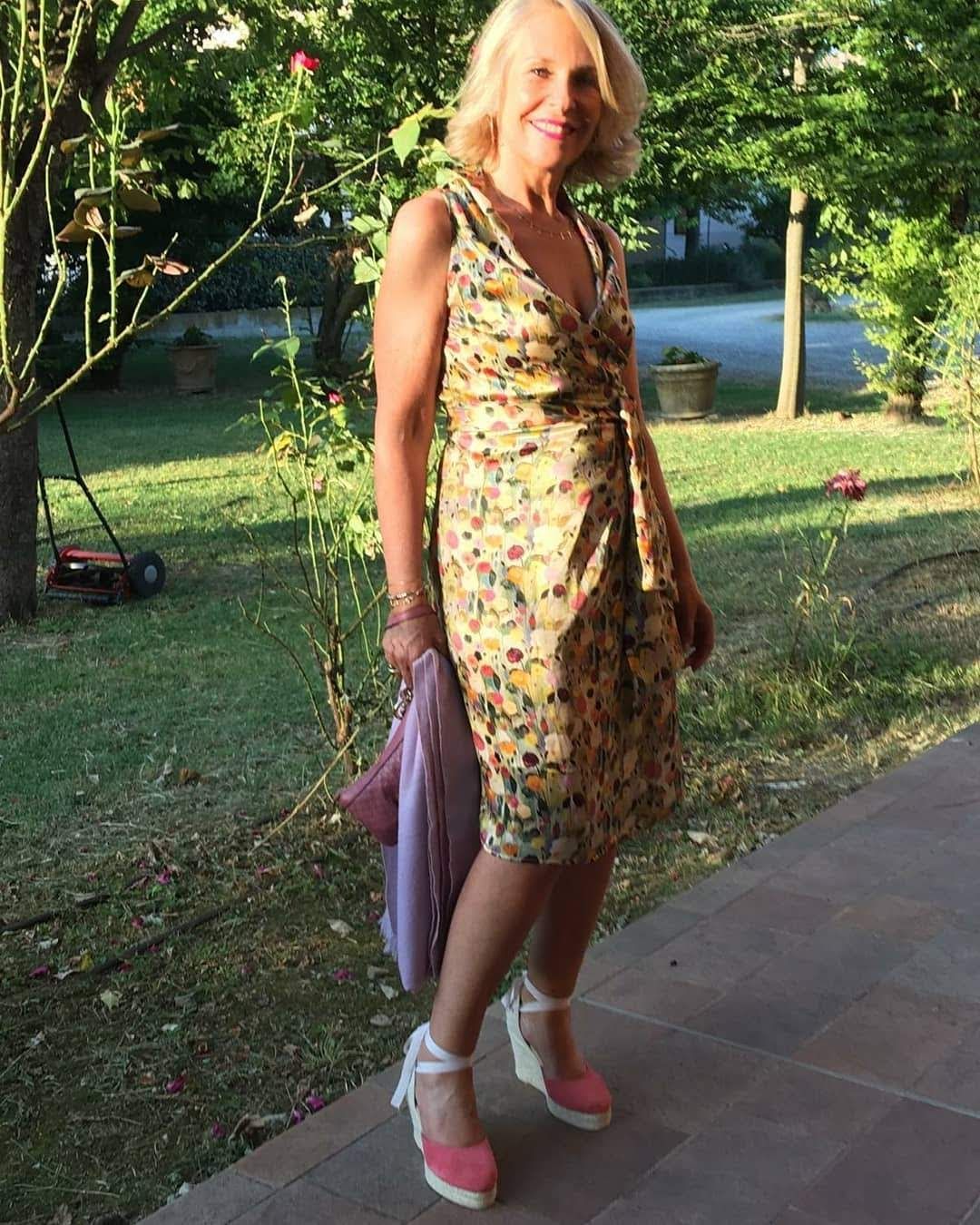 Una donna con un vestito giallo e scarpe rosa è in piedi sul marciapiede.