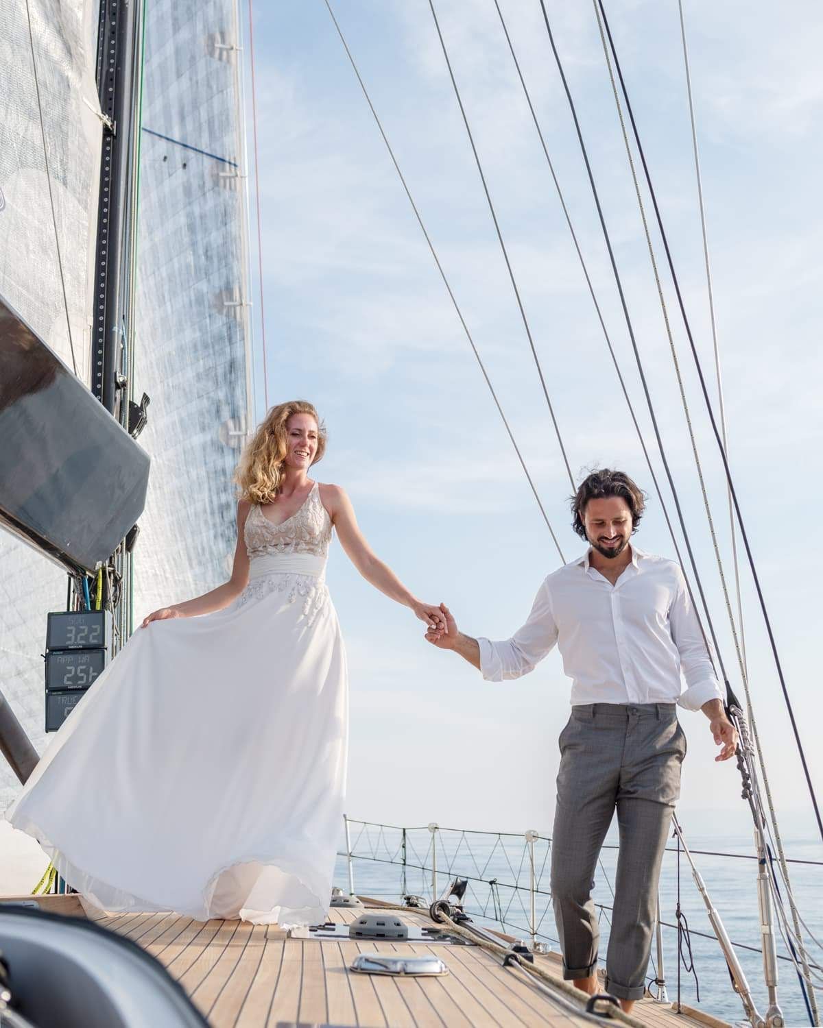 Una sposa e uno sposo si tengono per mano su una barca a vela.