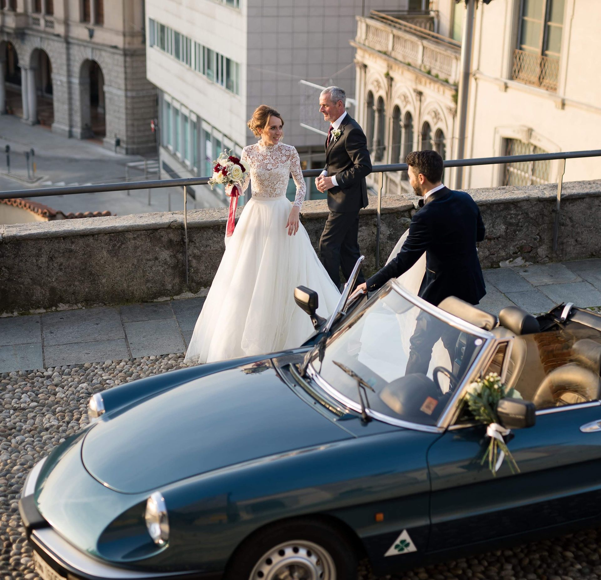 Una sposa e uno sposo sono in piedi accanto a un'auto blu