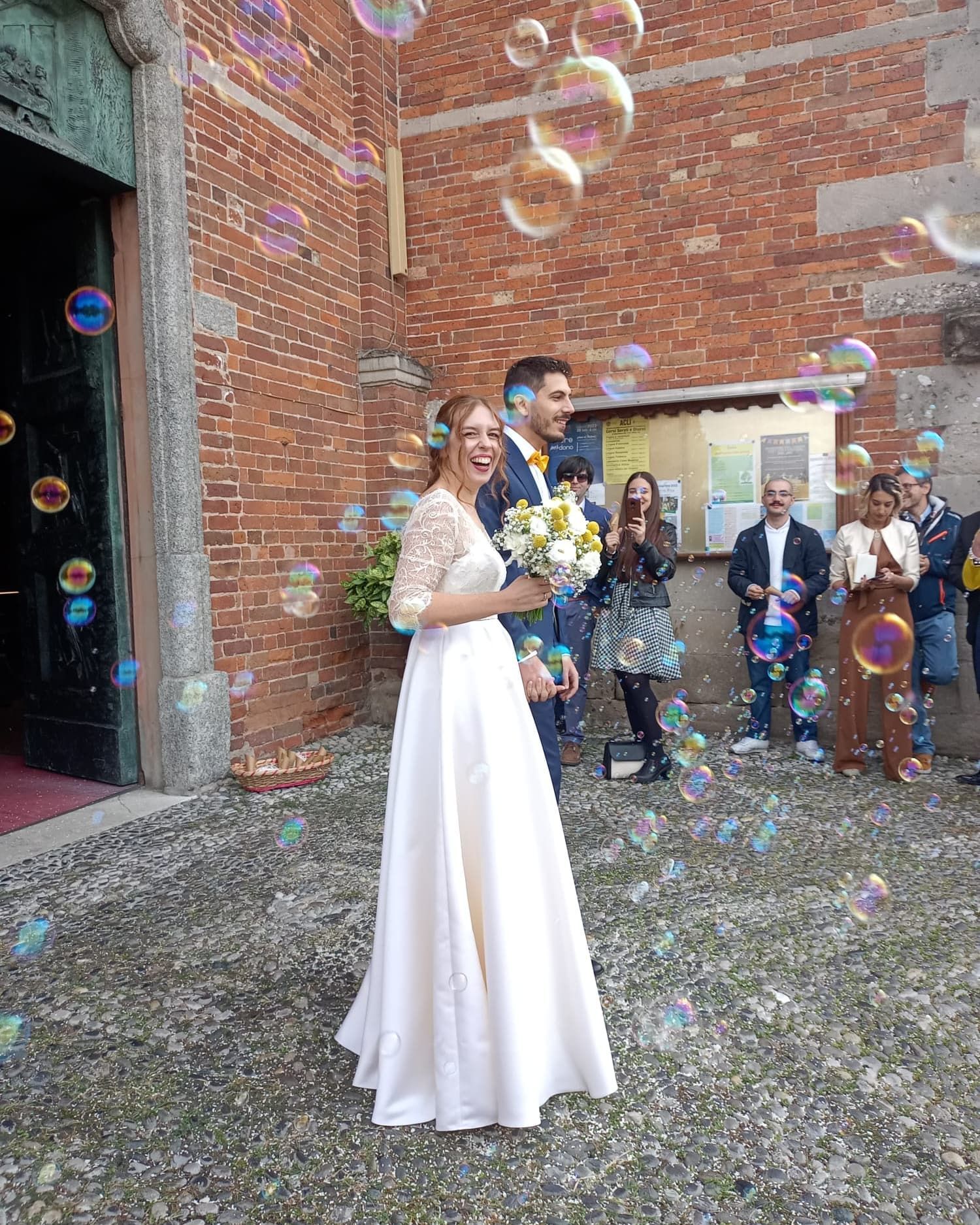 Una coppia di sposi è in piedi davanti a una chiesa, circondati da bolle di sapone.