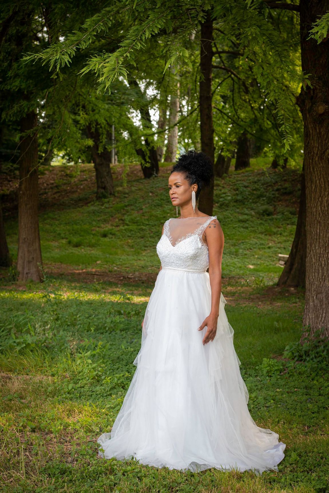 Una donna in abito da sposa è in piedi sull'erba in un parco.