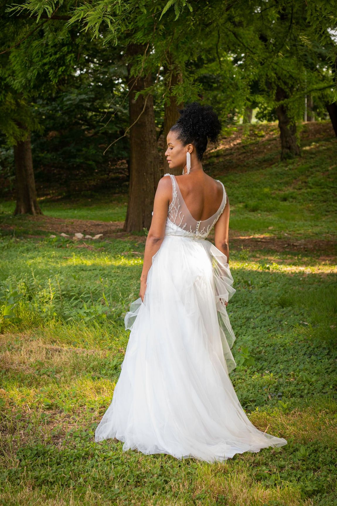 Una donna in abito da sposa è in piedi sull'erba in un parco.