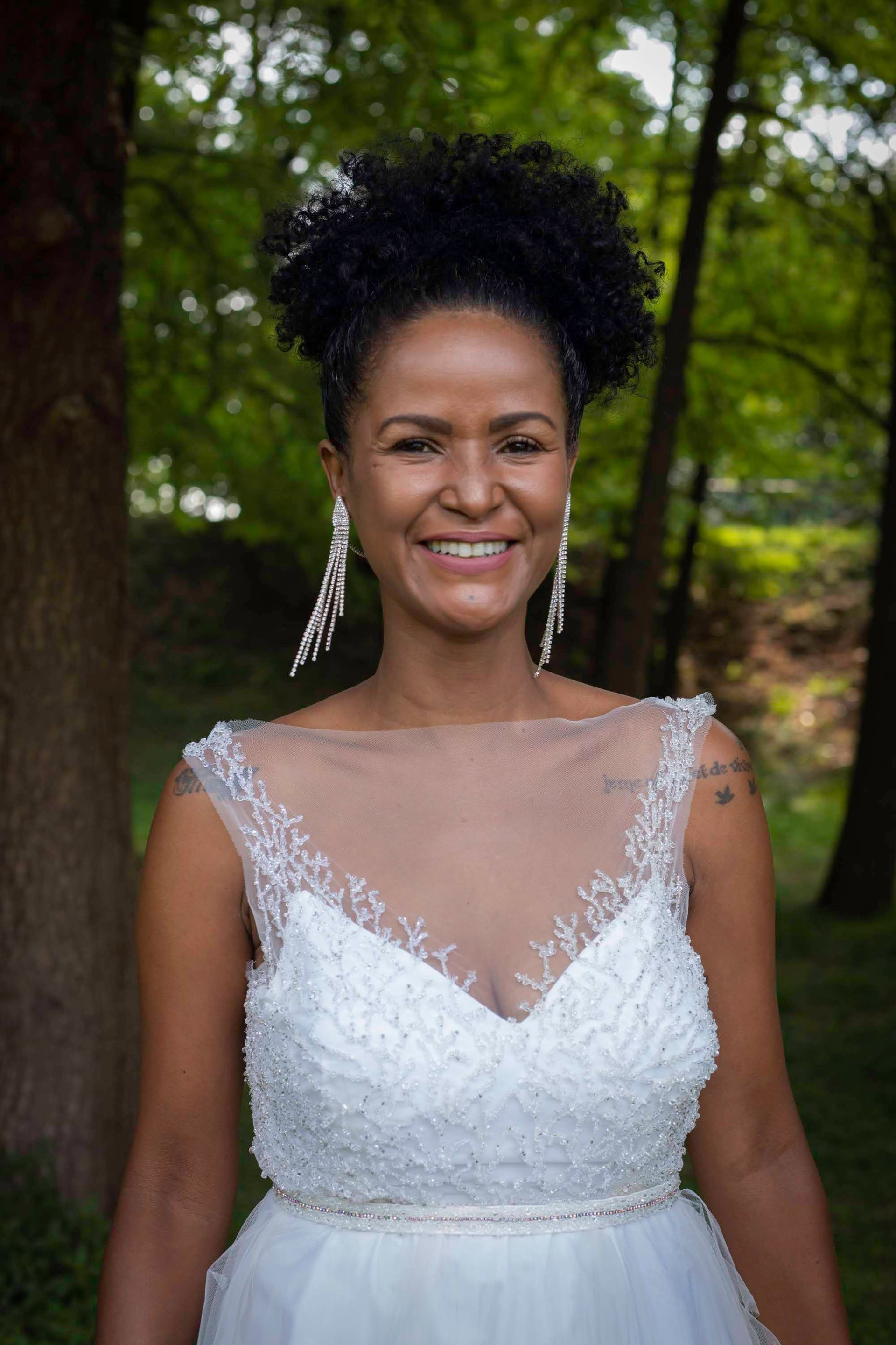 Una donna in abito da sposa sorride davanti a un albero.