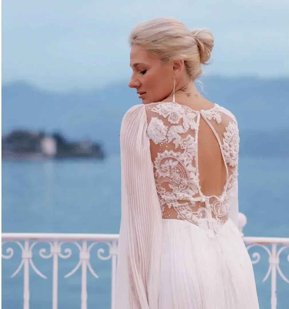 Una donna con un abito di pizzo bianco è in piedi su un balcone con vista sull'oceano