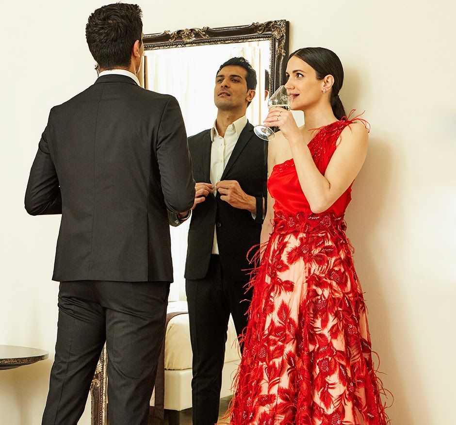 Un uomo in giacca e cravatta e una donna in abito rosso sono in piedi davanti a uno specchio