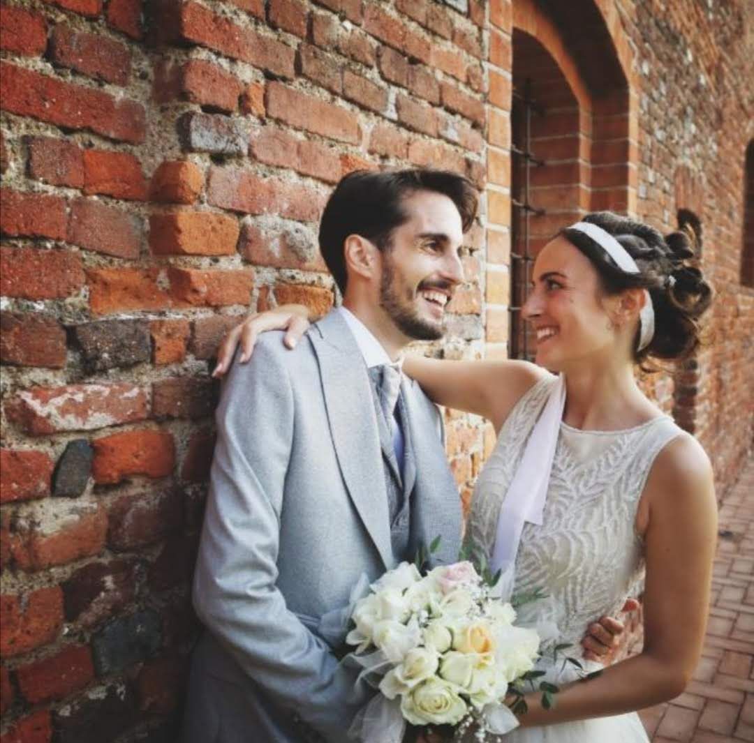 Una sposa e uno sposo posano per una foto davanti a un muro di mattoni