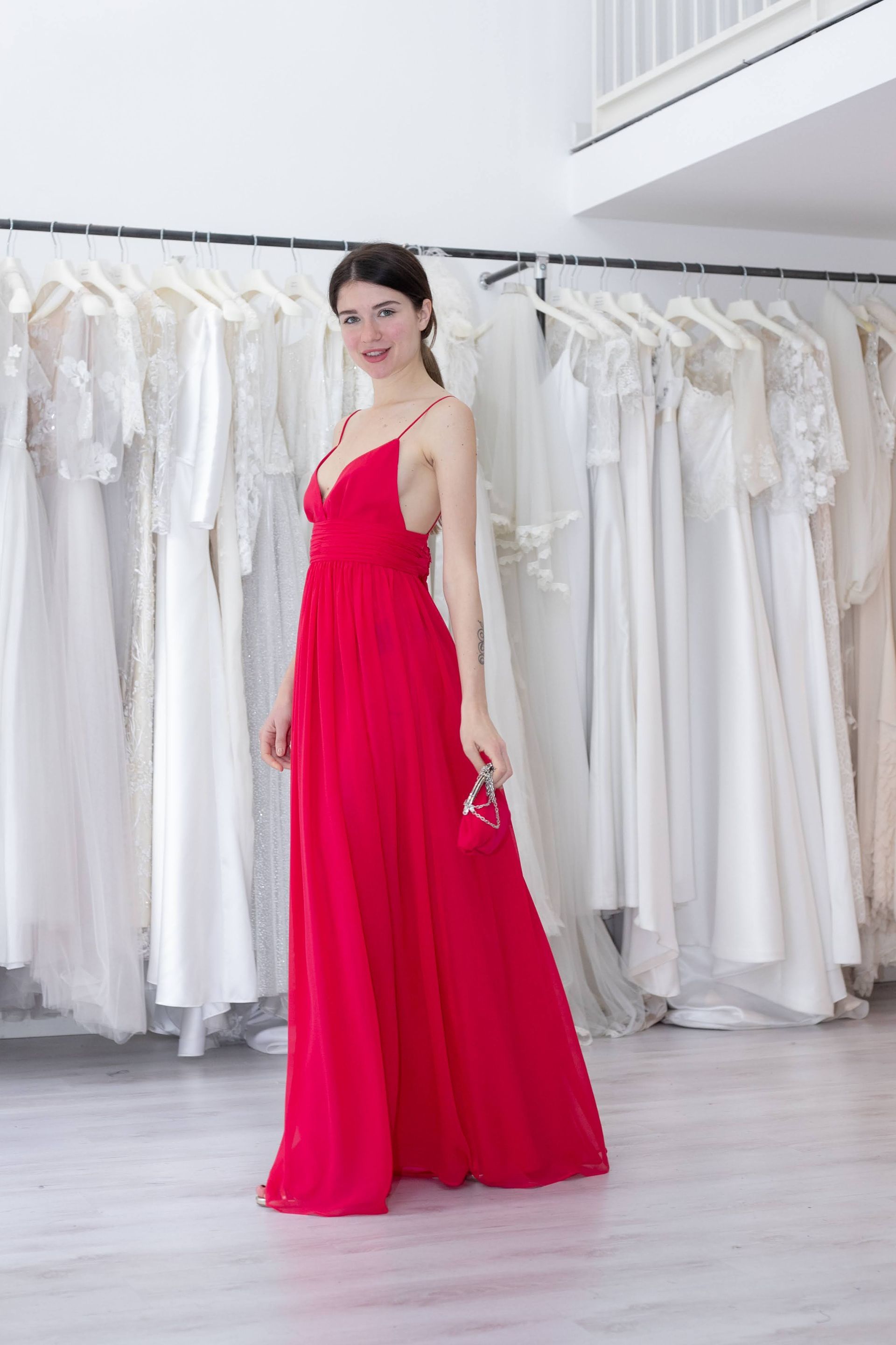 Una donna con un vestito rosso è in piedi davanti a uno scaffale di vestiti bianchi.