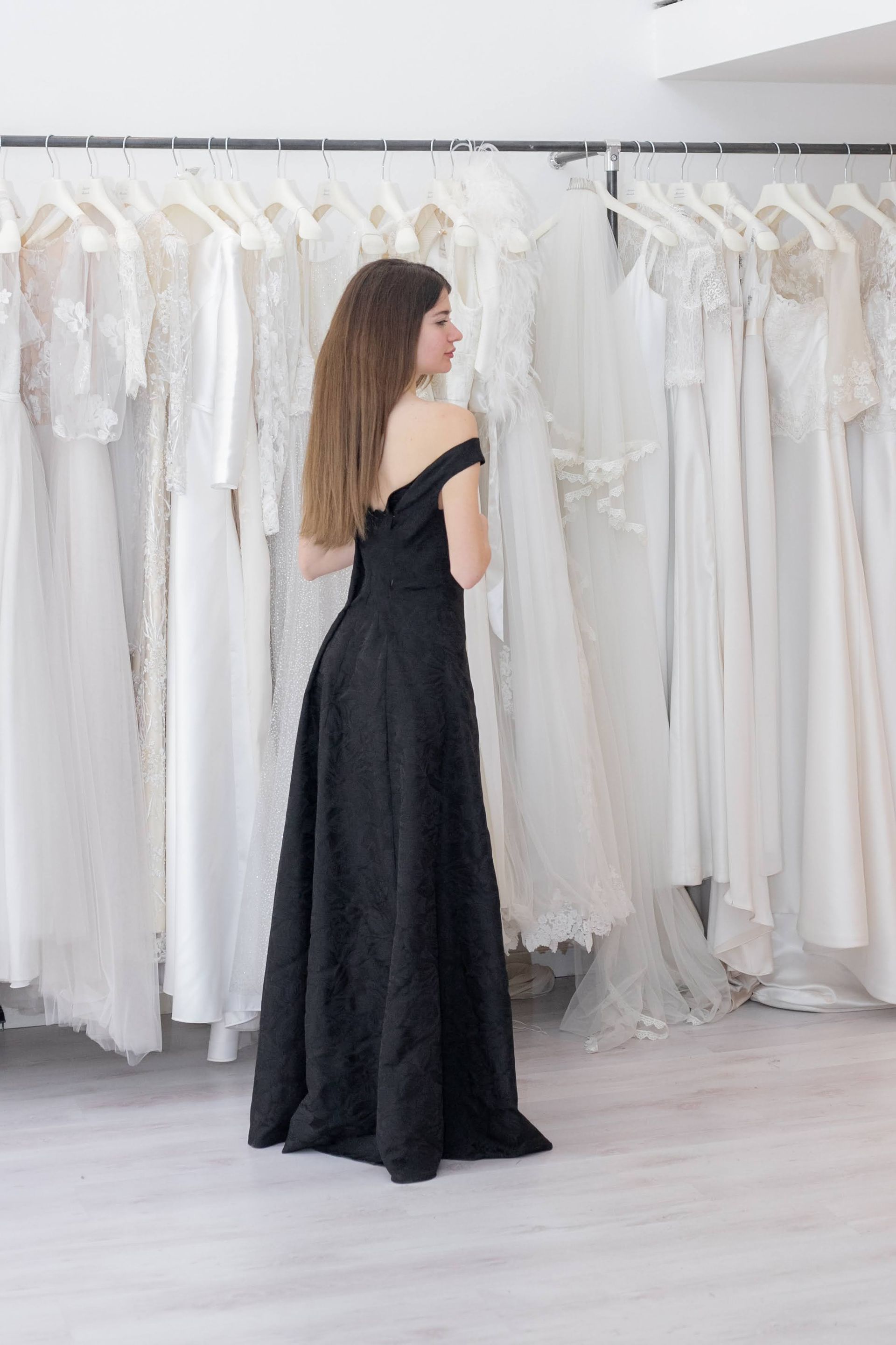 Una donna con un abito nero è in piedi davanti a una fila di abiti bianchi.