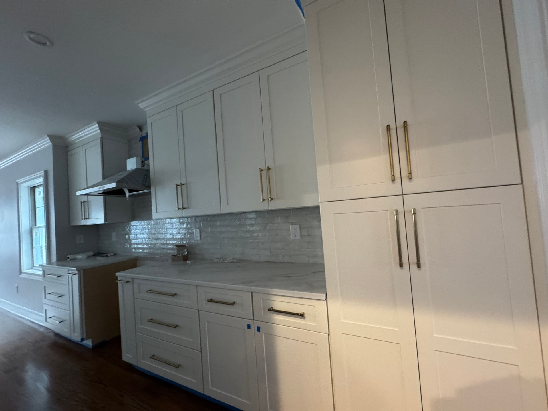Bright white kitchen with gray backsplash, stainless range hood, and built-in cabinets along a hallway.