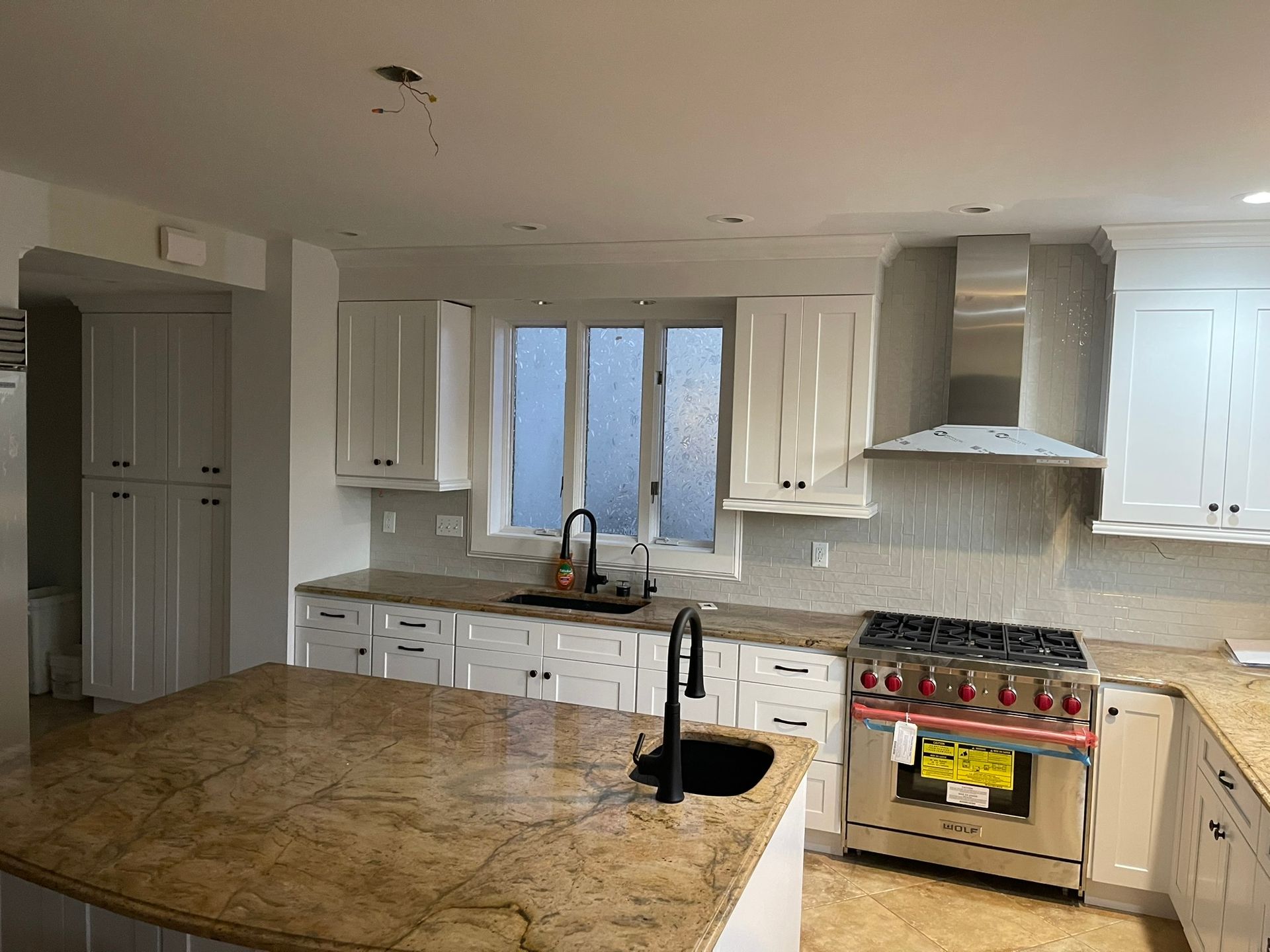 Bright modern kitchen with white cabinets, granite island, stainless stove, and large window above sink