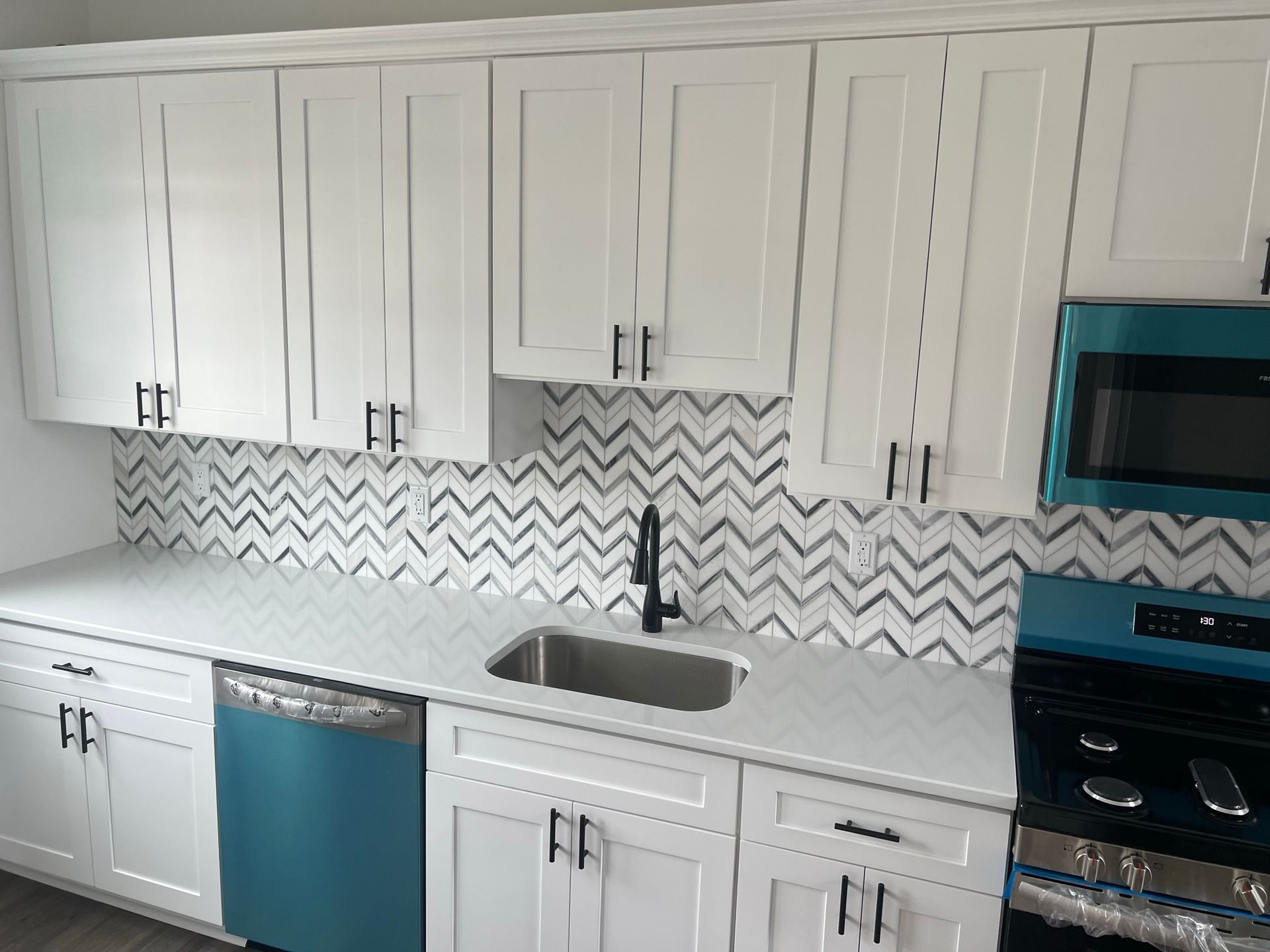 Modern white kitchen with teal appliances, herringbone backsplash, and black faucet sink