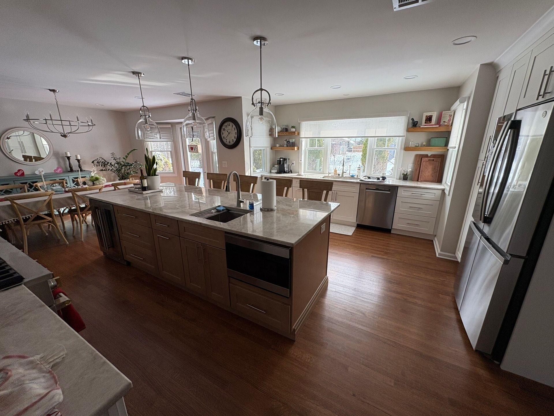 Bright modern kitchen with a large island, white cabinets, wood floors, and a refrigerator by the wall