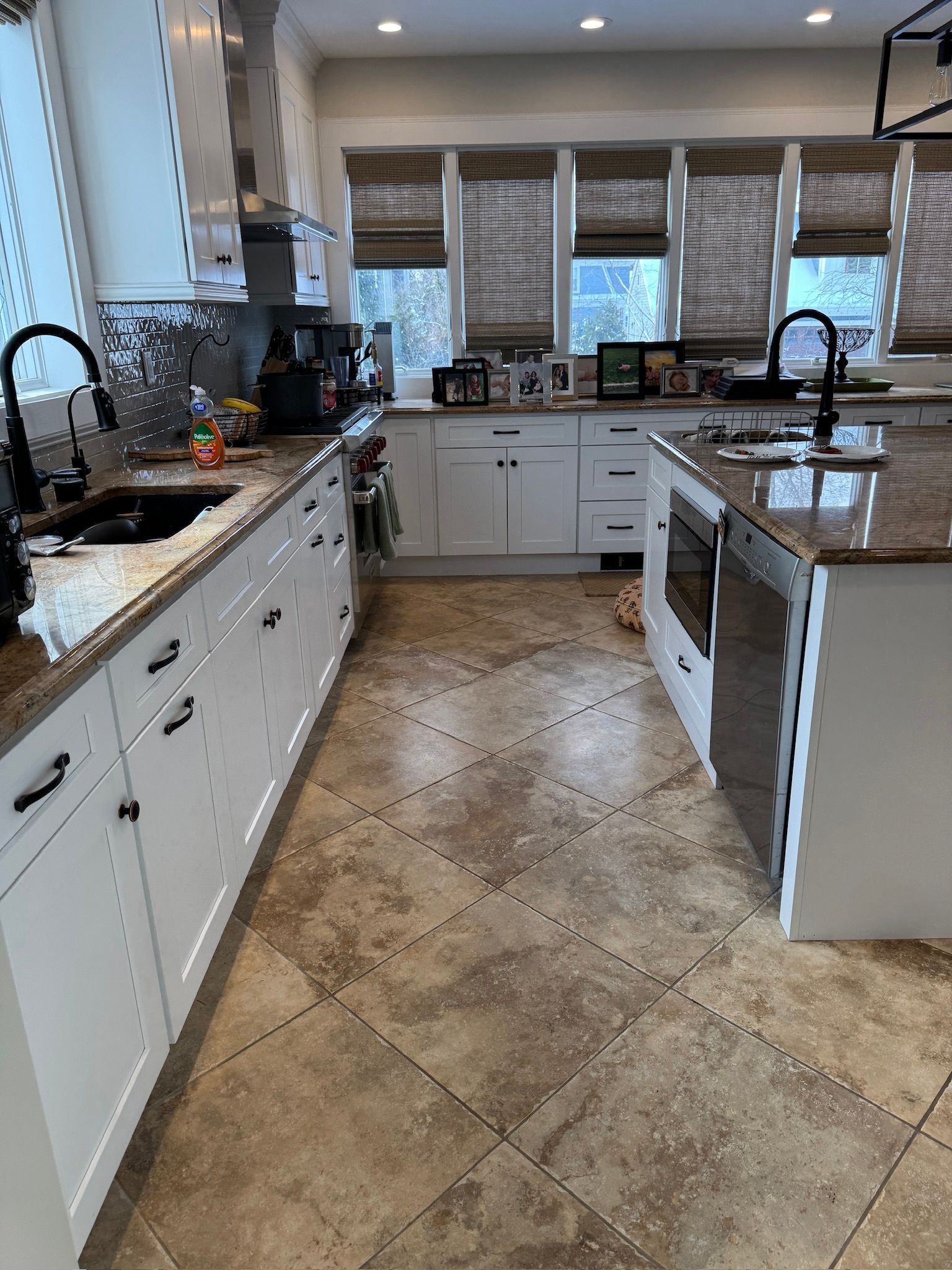 Bright white kitchen with marble countertops, tile floor, island, and window blinds over the sink.