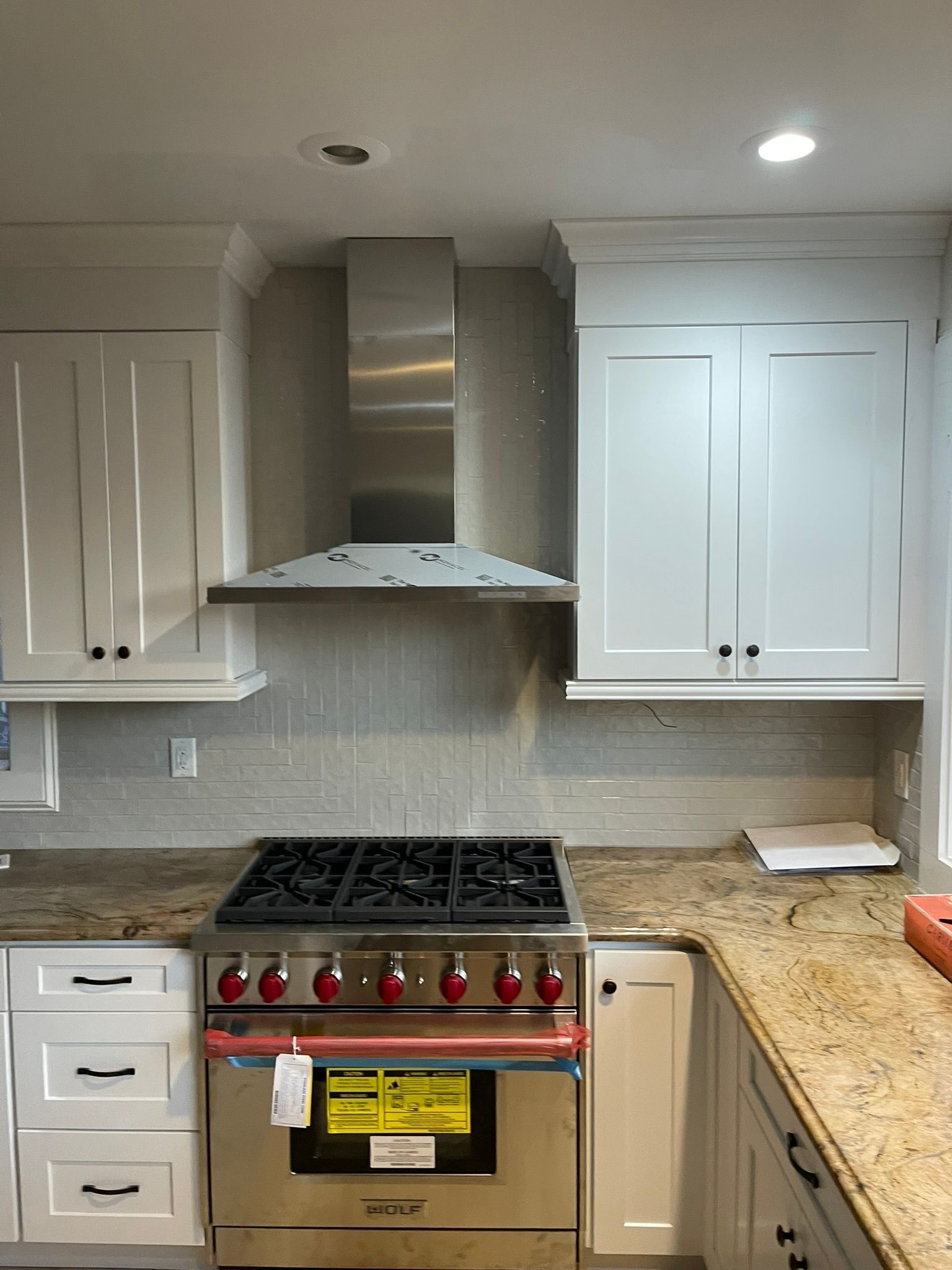 Modern kitchen with white cabinets, stainless range hood, gas stove, and granite countertops