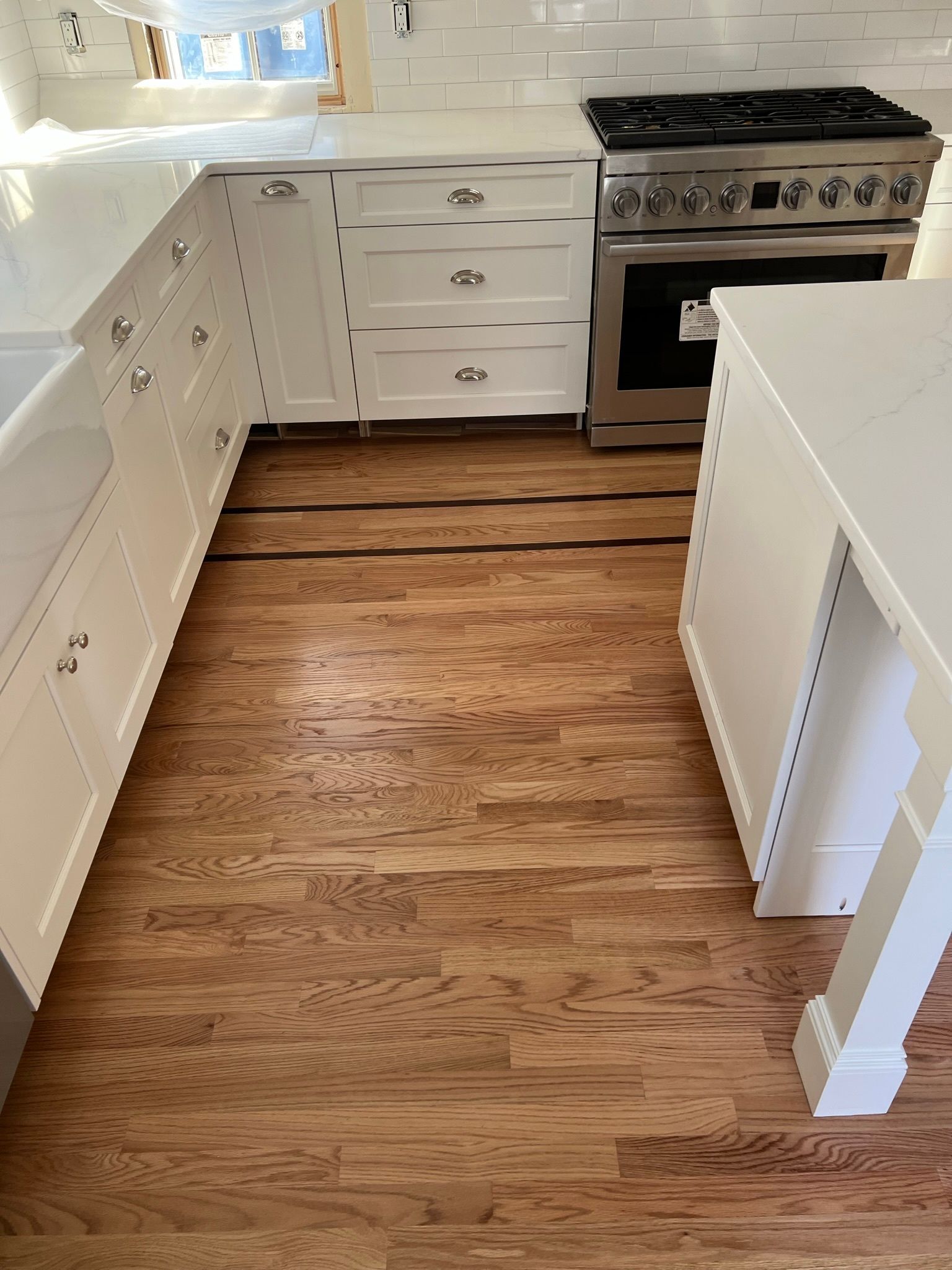 Narrow kitchen walkway with wood floor, white cabinets, and a stainless steel stove