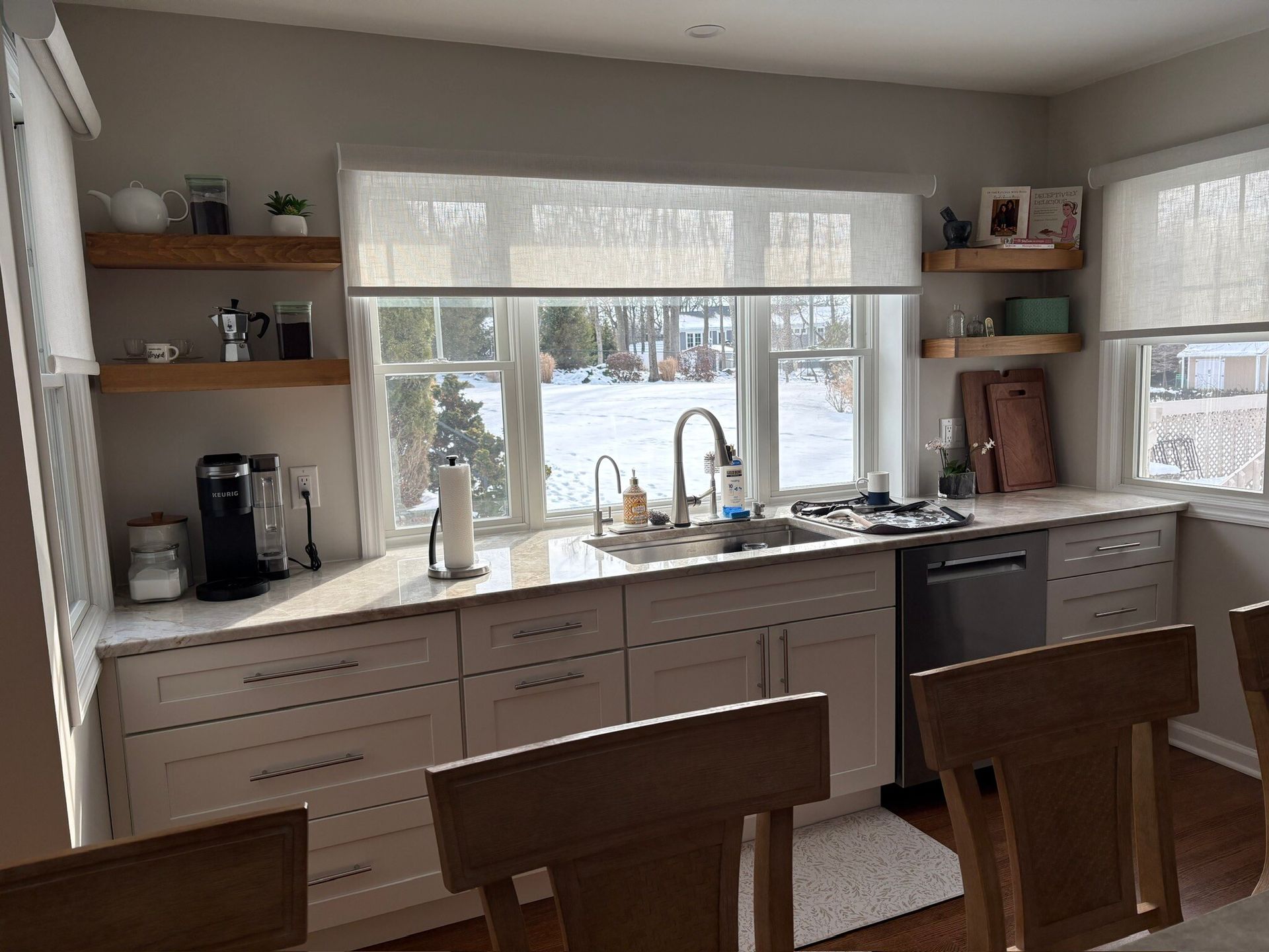 Modern kitchen with large window, wooden cabinets, island stools, sink, and coffee maker