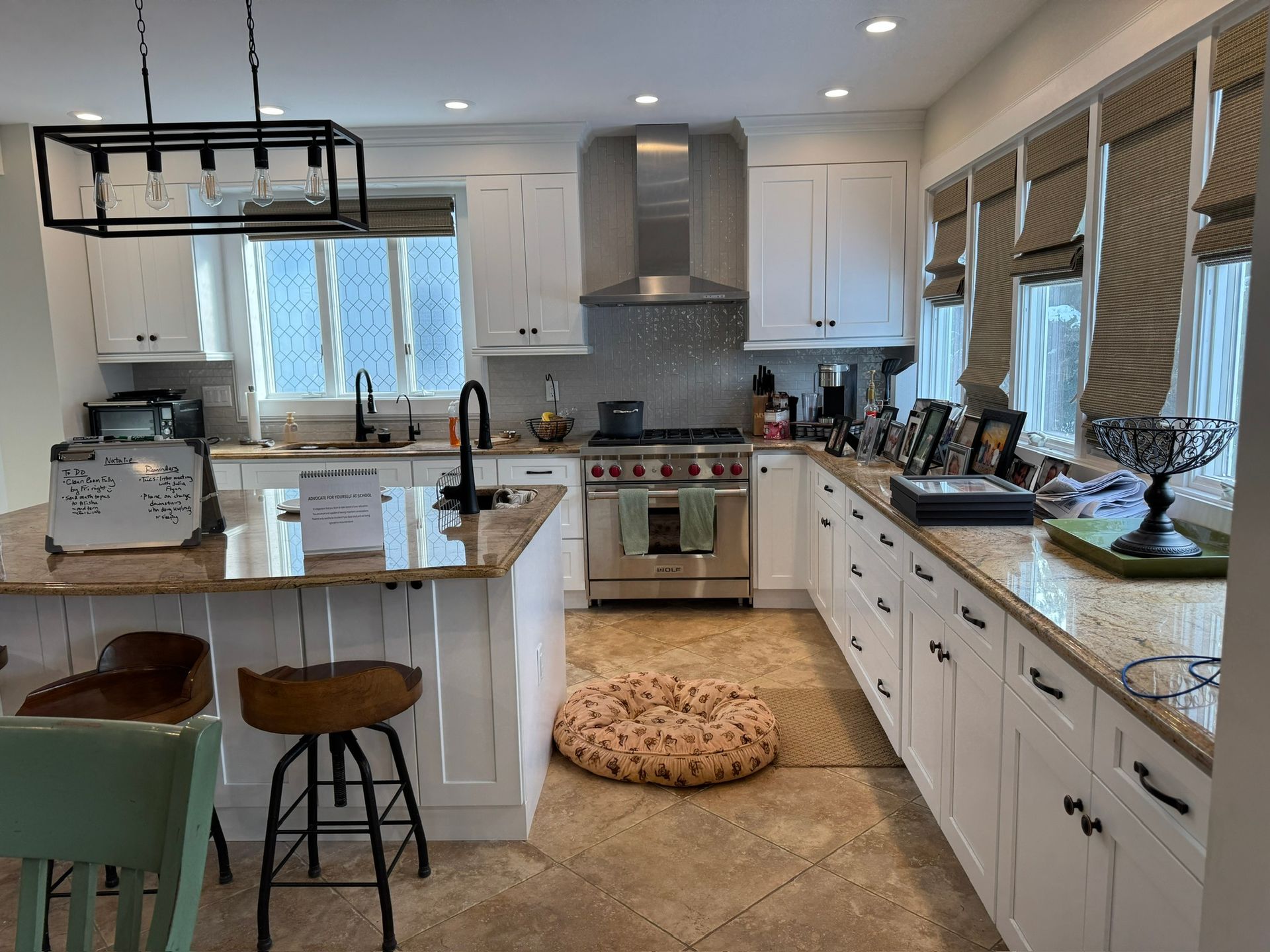 Modern white kitchen with island, stainless range, large windows, and a round dog bed on the floor