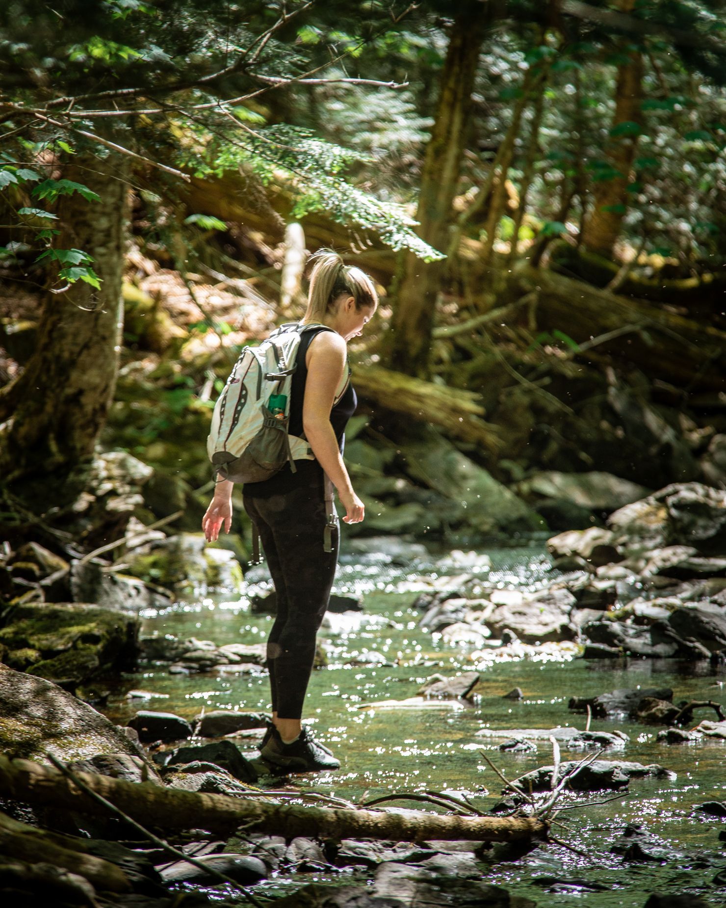 Woman with backpack hikes through a stream in a forest.