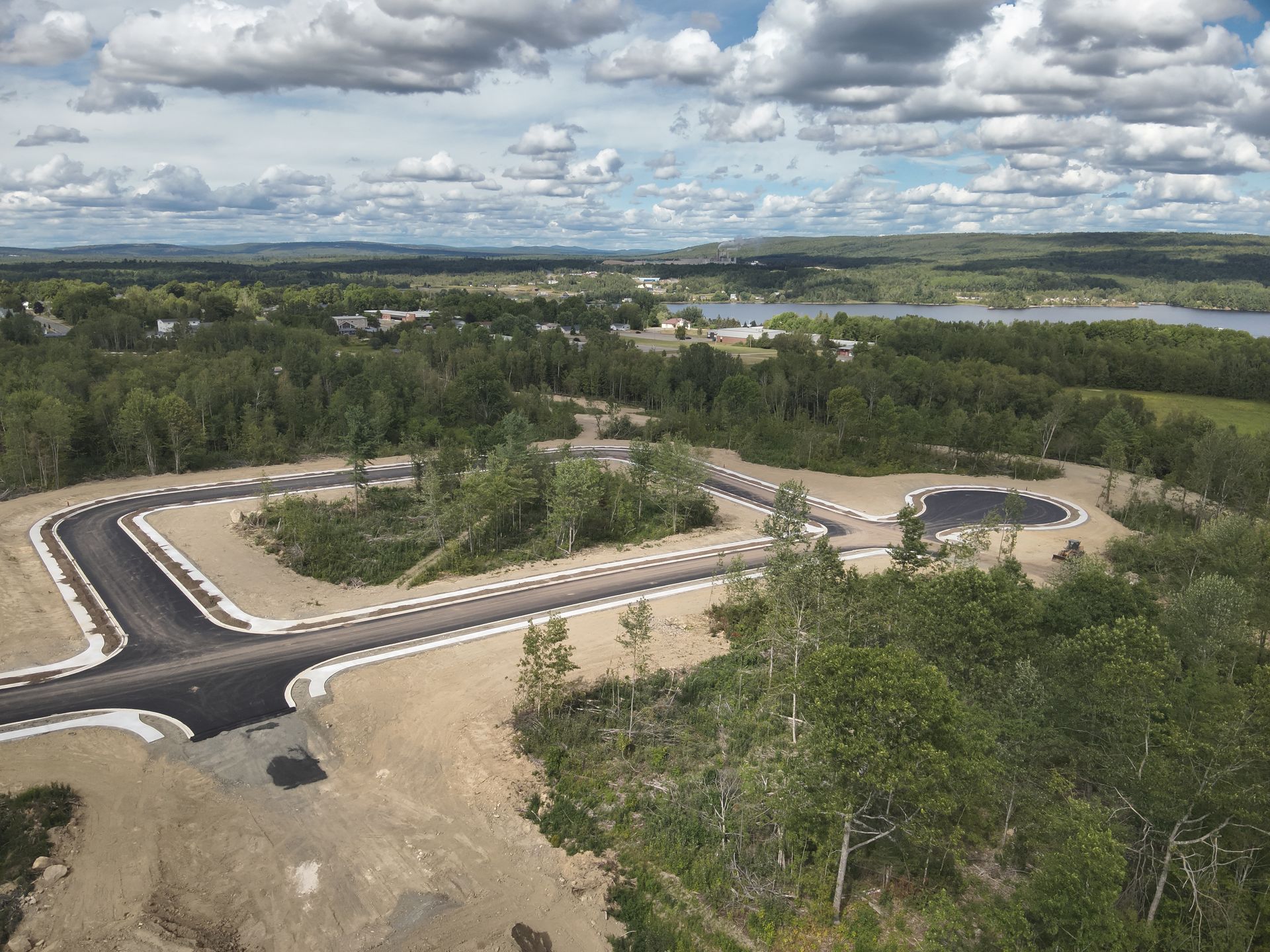 An aerial view of a new residential development under construction with paved roads set against a wooded landscape.